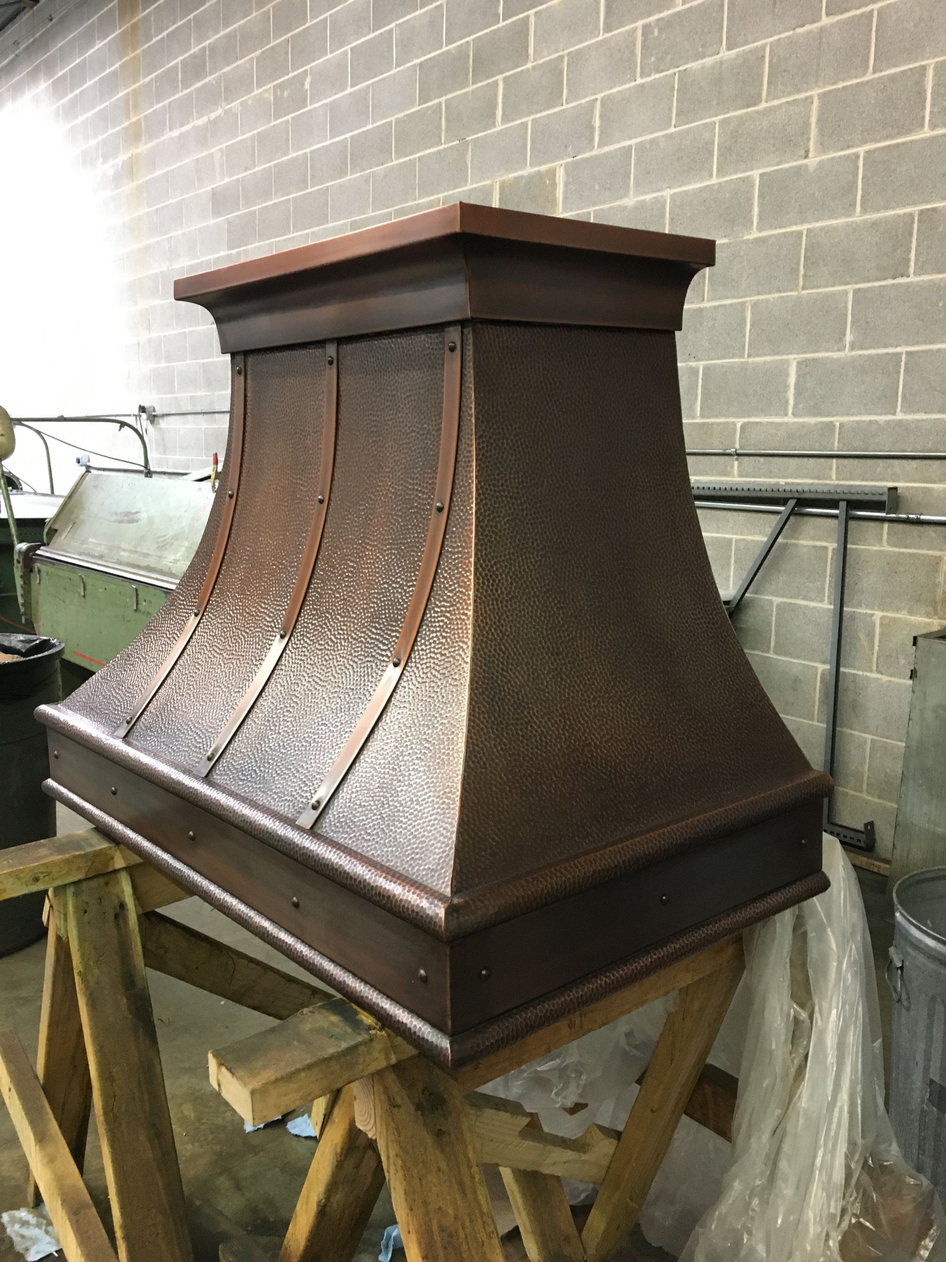 Rusty metal chimney hood on a wooden stand beside a brick wall.