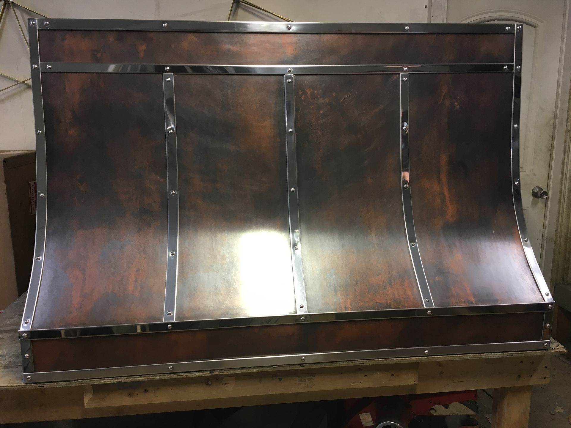Copper-toned metal hood or backsplash panel on a workbench, with curved sides and riveted seams