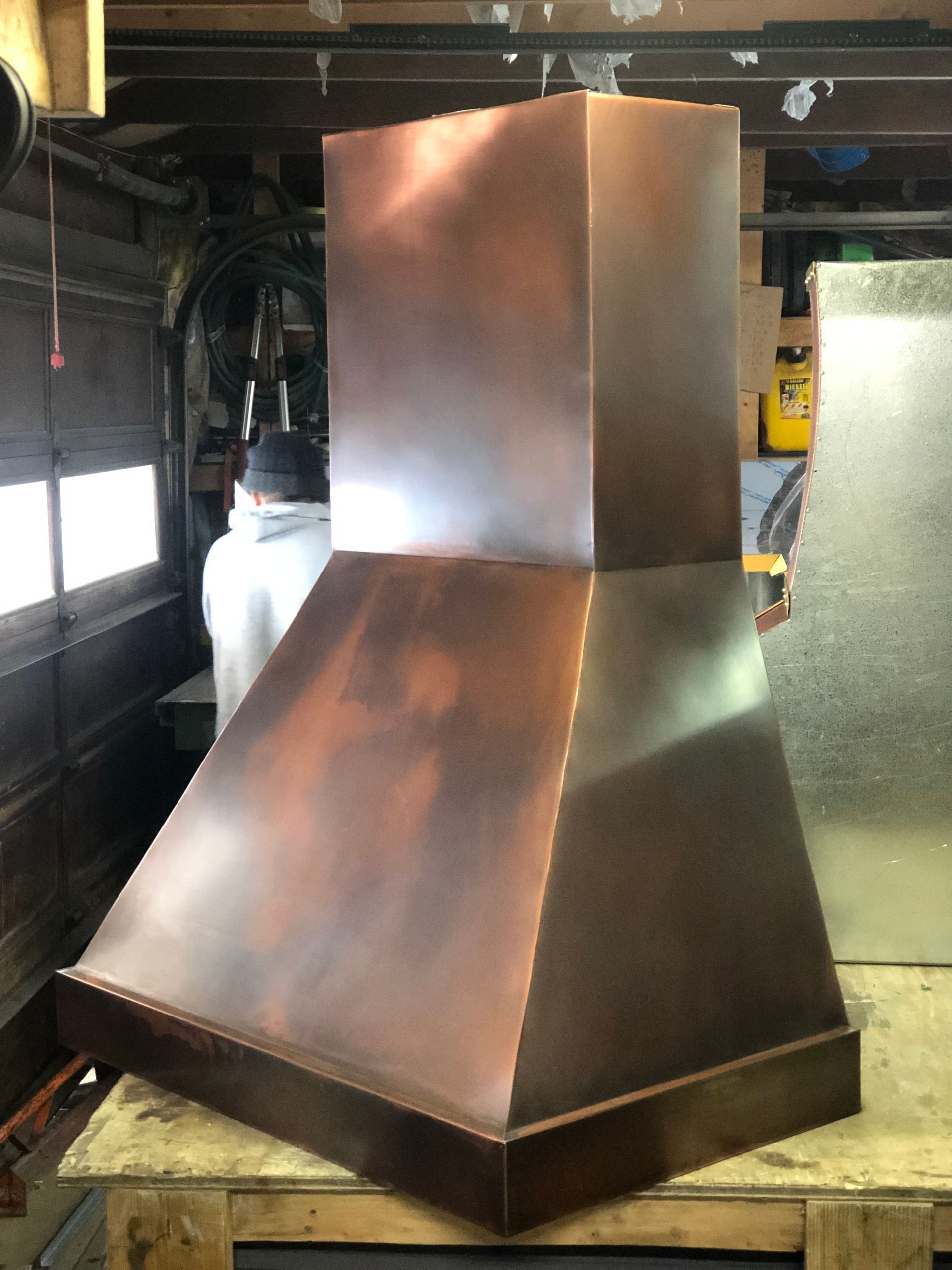 Copper-colored industrial hood or exhaust chimney in a workshop, with a square top and sloped base.