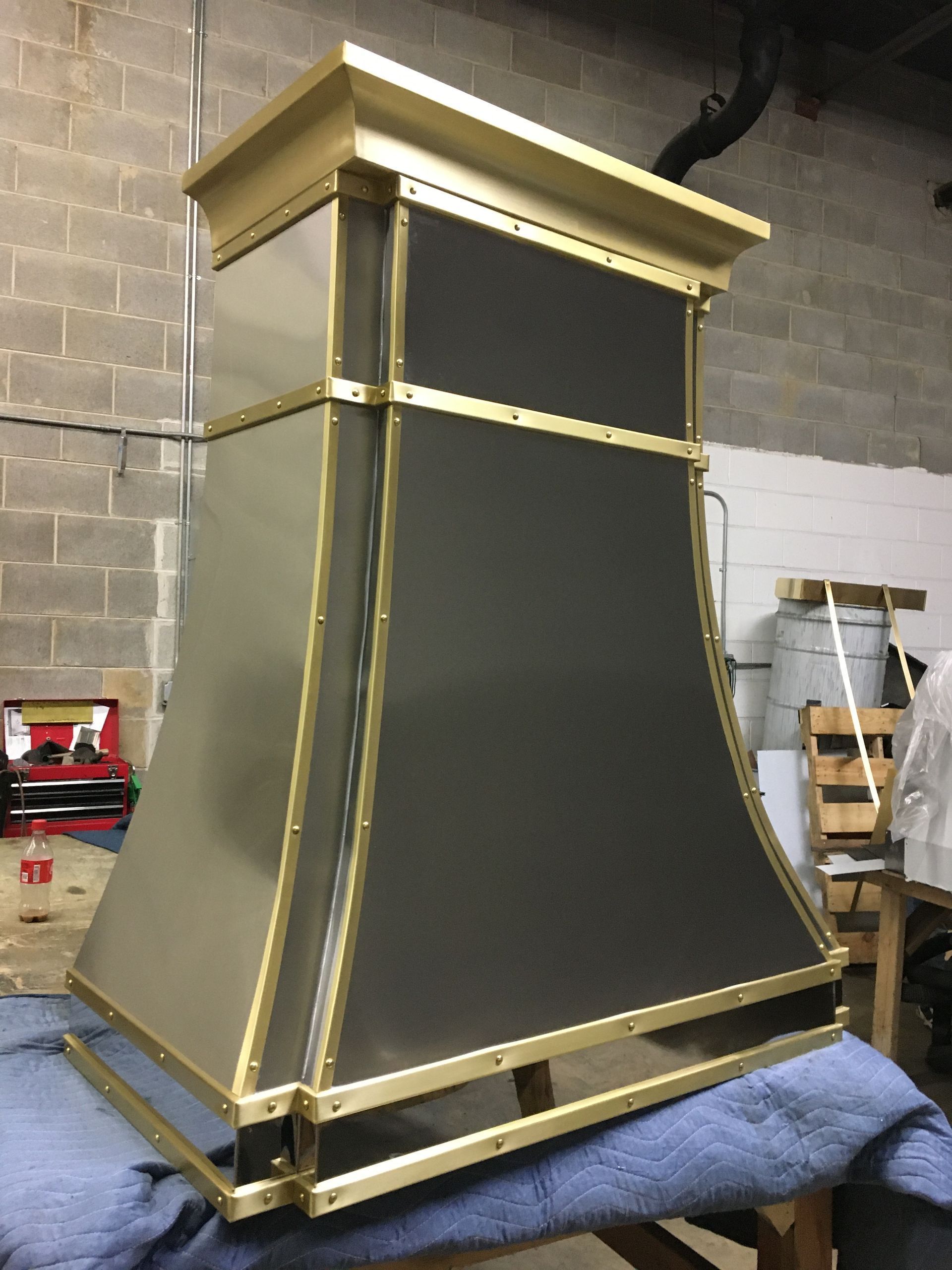 Gold-trimmed black fireplace mantel standing in a warehouse workshop with cinder block walls.