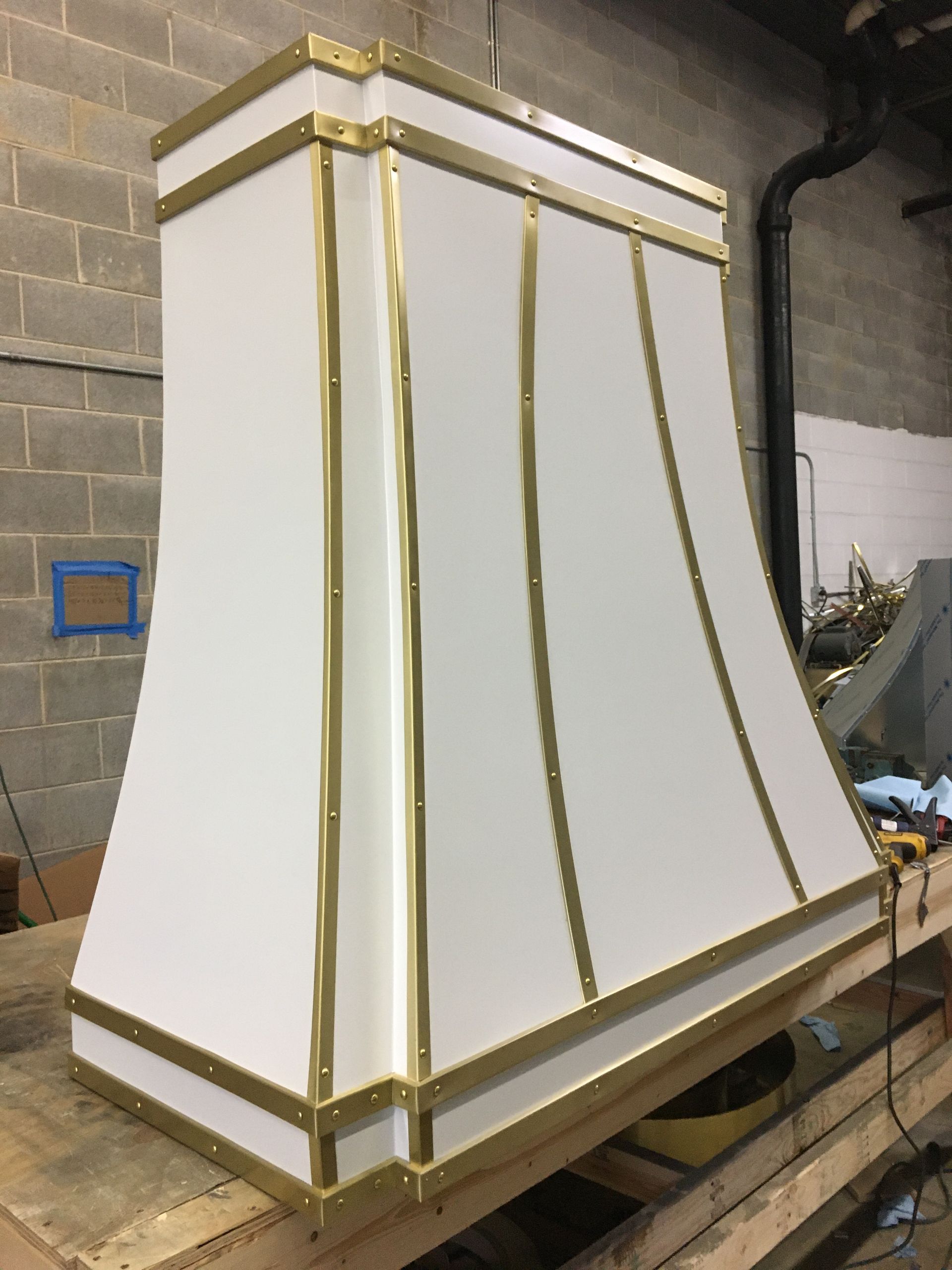 White tapered industrial hood with gold trim in a workshop or storage area