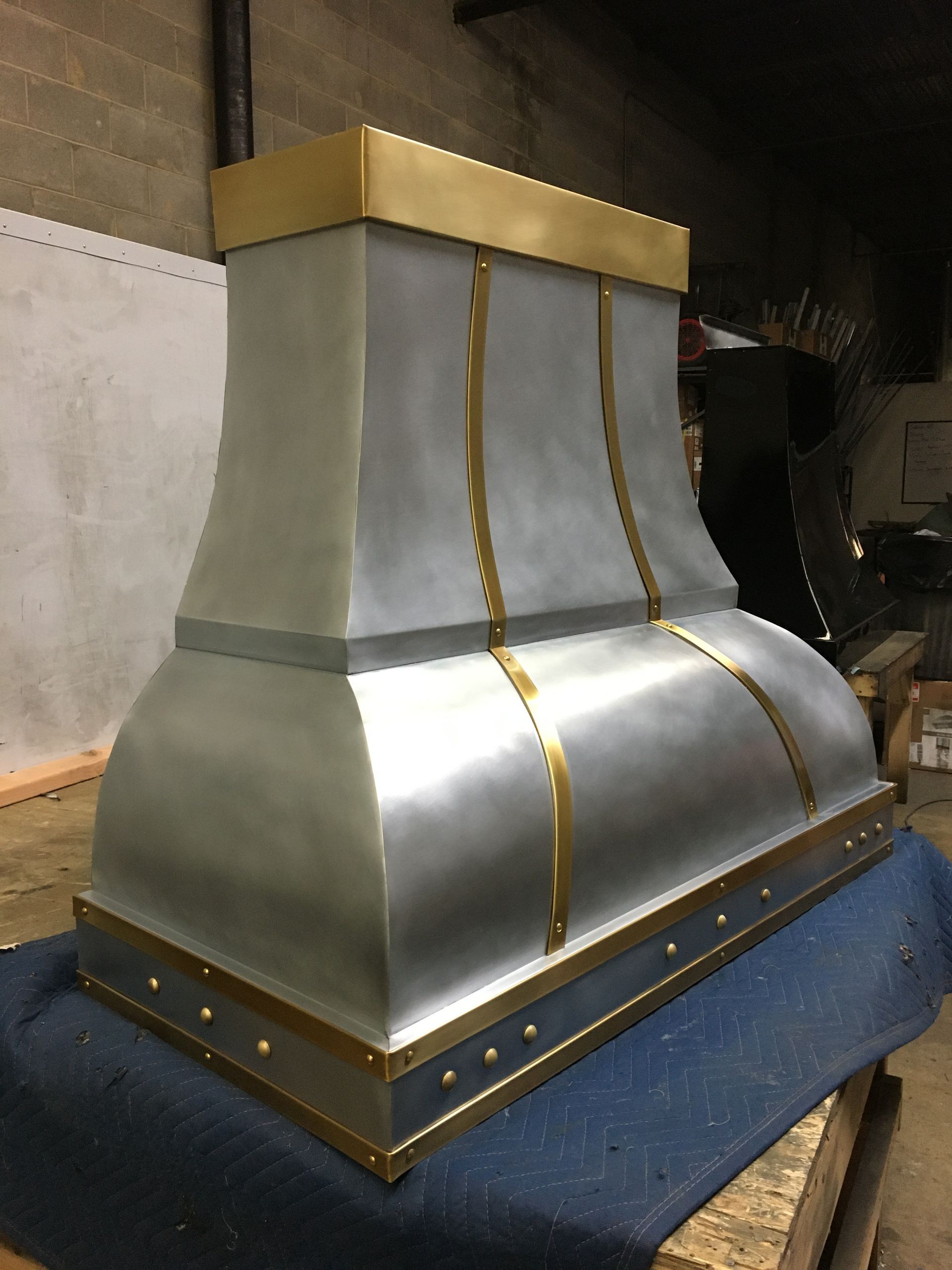 Metallic chimney or hood with gold trim on a blue base, indoors against a concrete wall