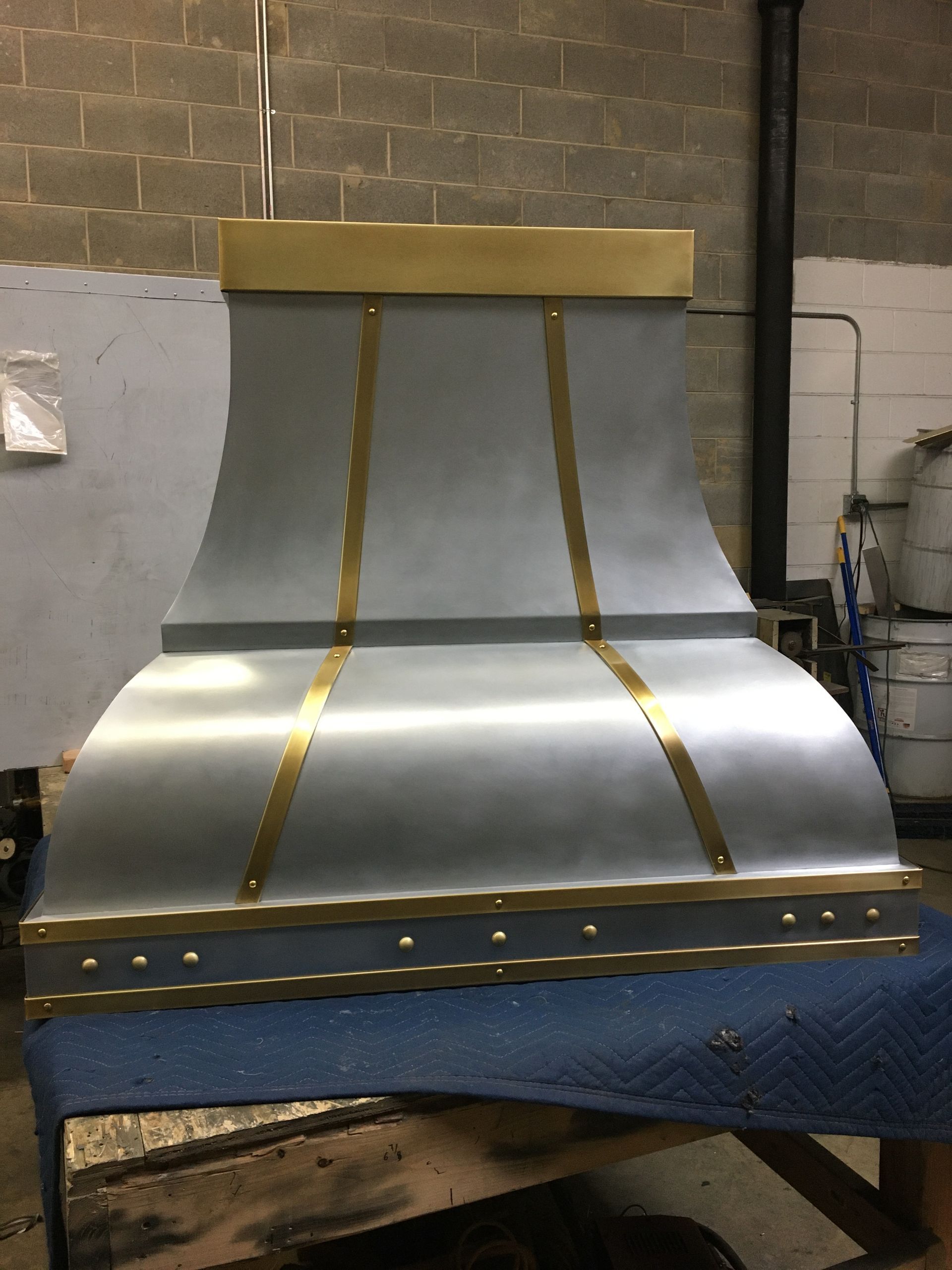 Metal duct or hood prototype with gold trim on a blue workbench in an industrial workshop