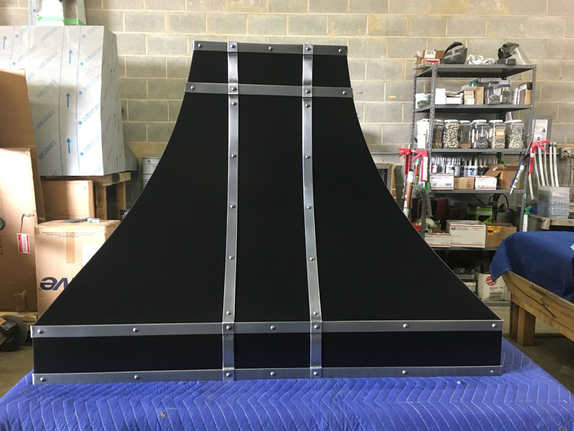 Black metal ramp or skate obstacle in a workshop, with silver support bars and a blue padded base.