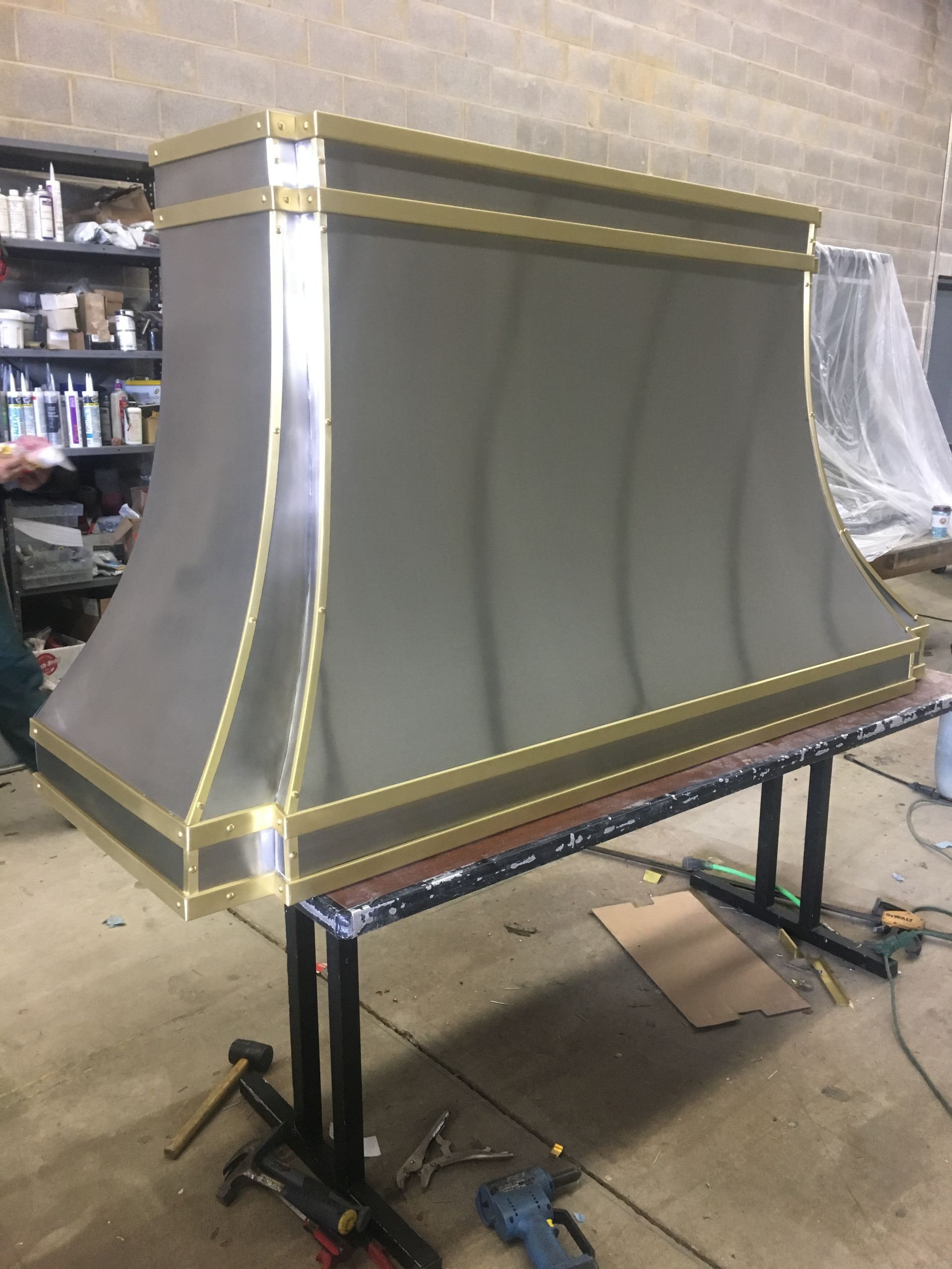Large gray upholstered furniture piece with gold trim on a workshop stand in a garage.