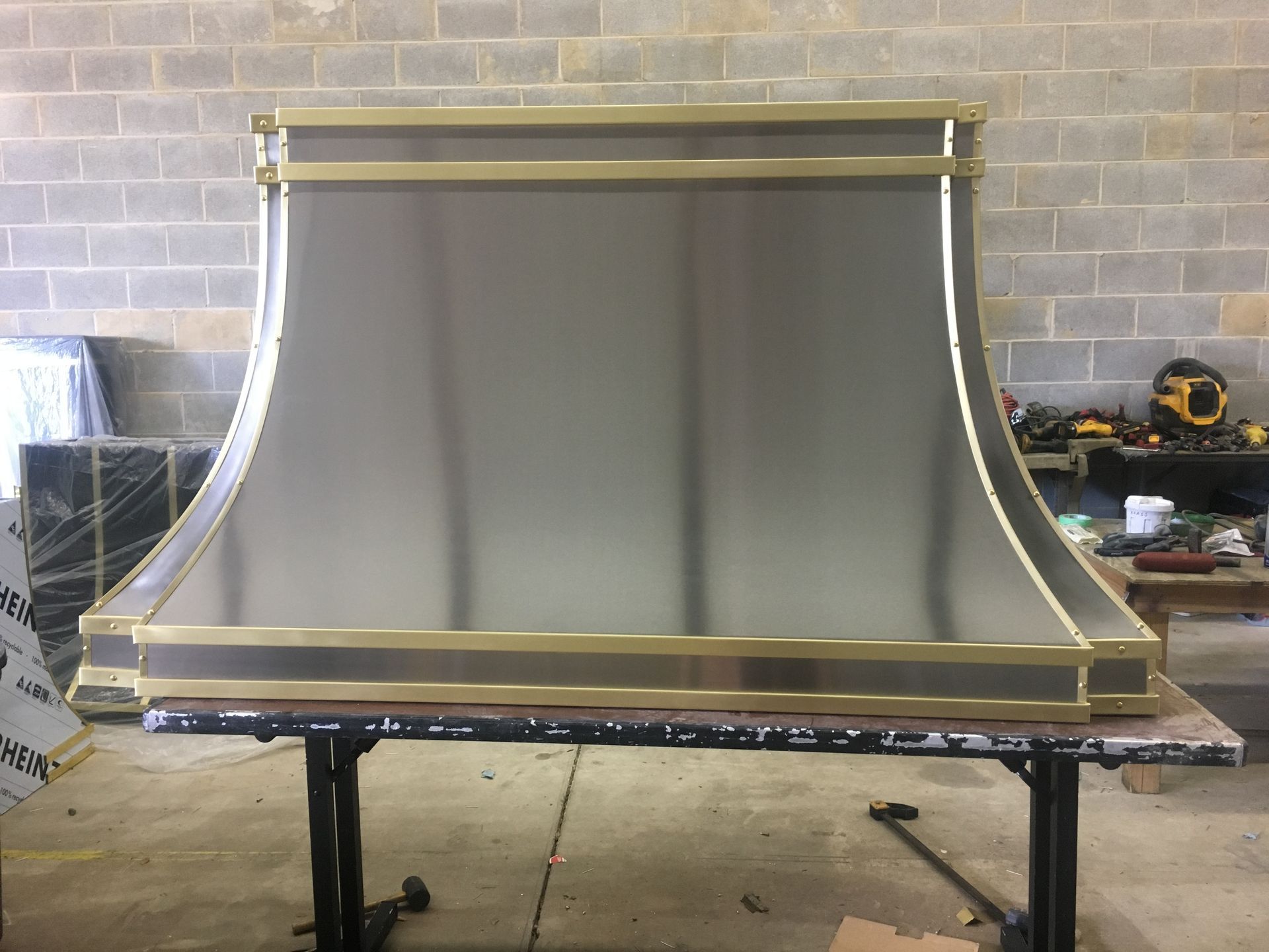 Large gray curved metal panel with gold trim on a workshop table in a garage