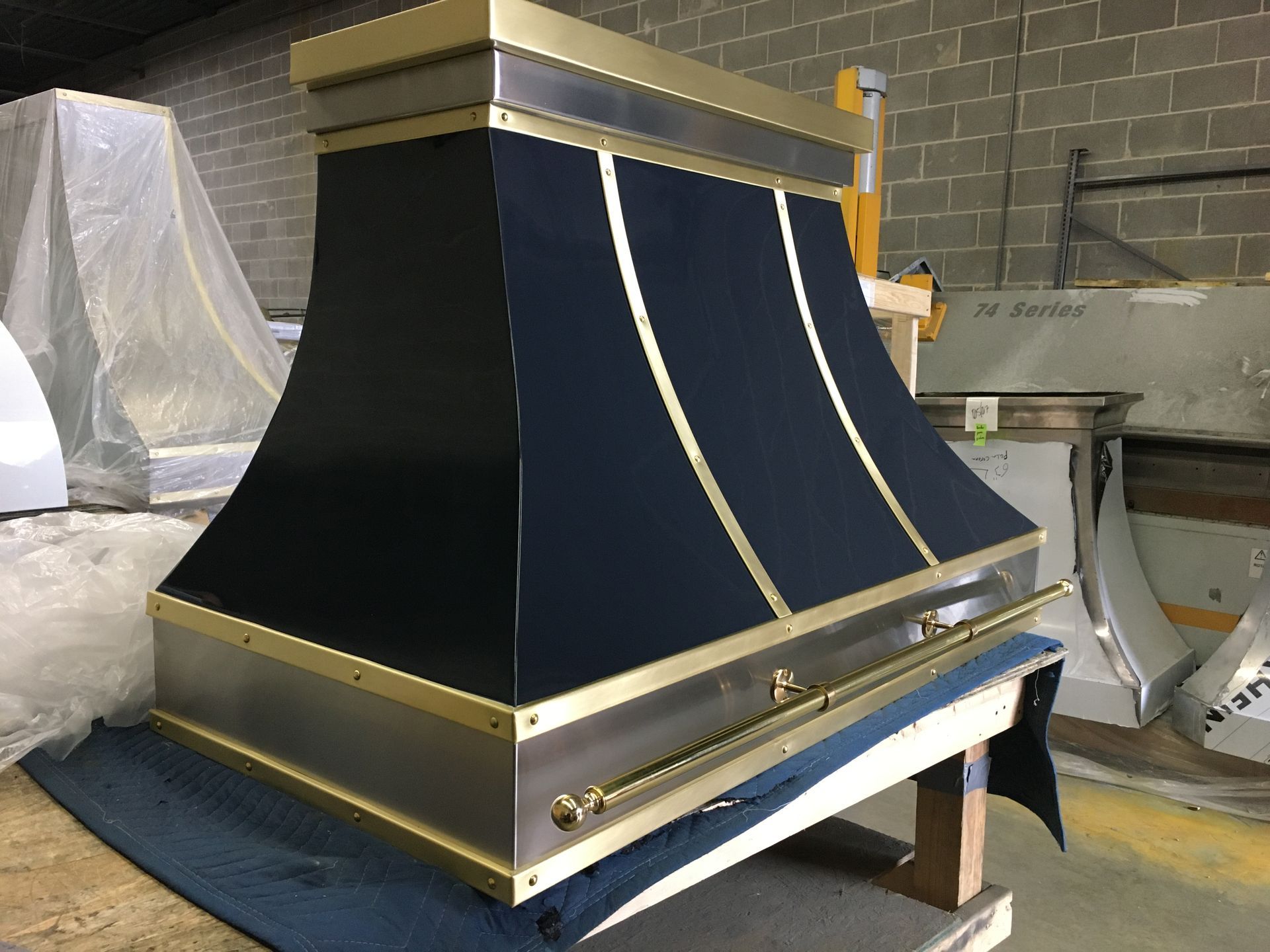 Large black-and-gold industrial hood or vent assembly in a workshop, with curved front panels and metal trim