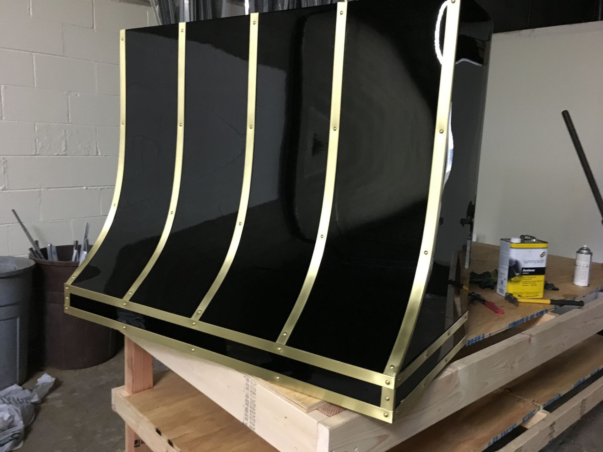 Black curved panel with pale yellow supports on a wooden platform in a workshop
