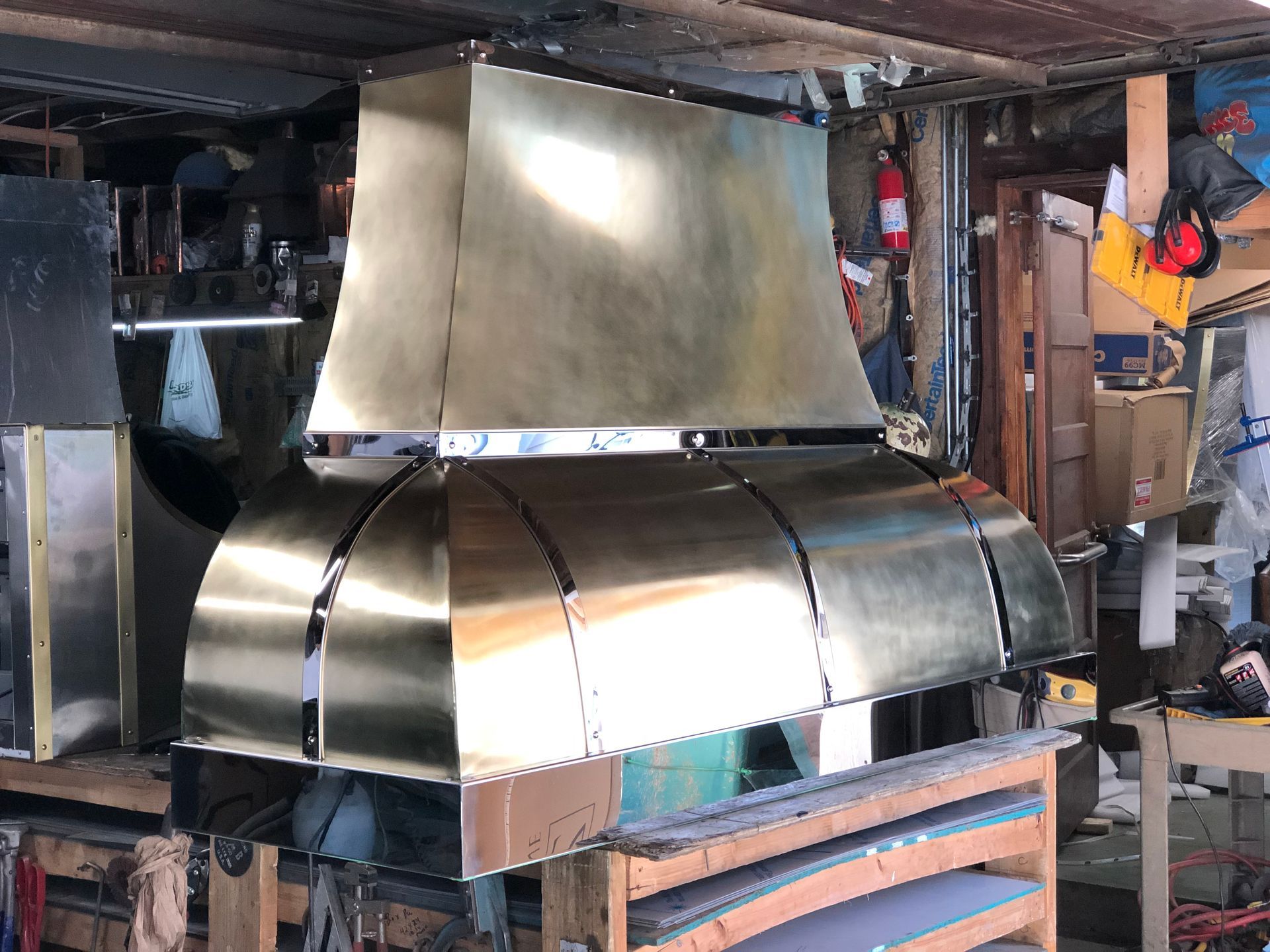 Shiny metal industrial hood or vent assembly in a workshop, partially assembled on a pallet.