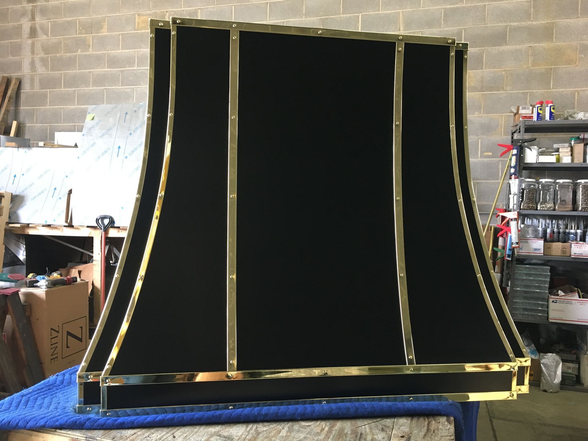 Black curved panel with gold trim standing in a workshop or garage.