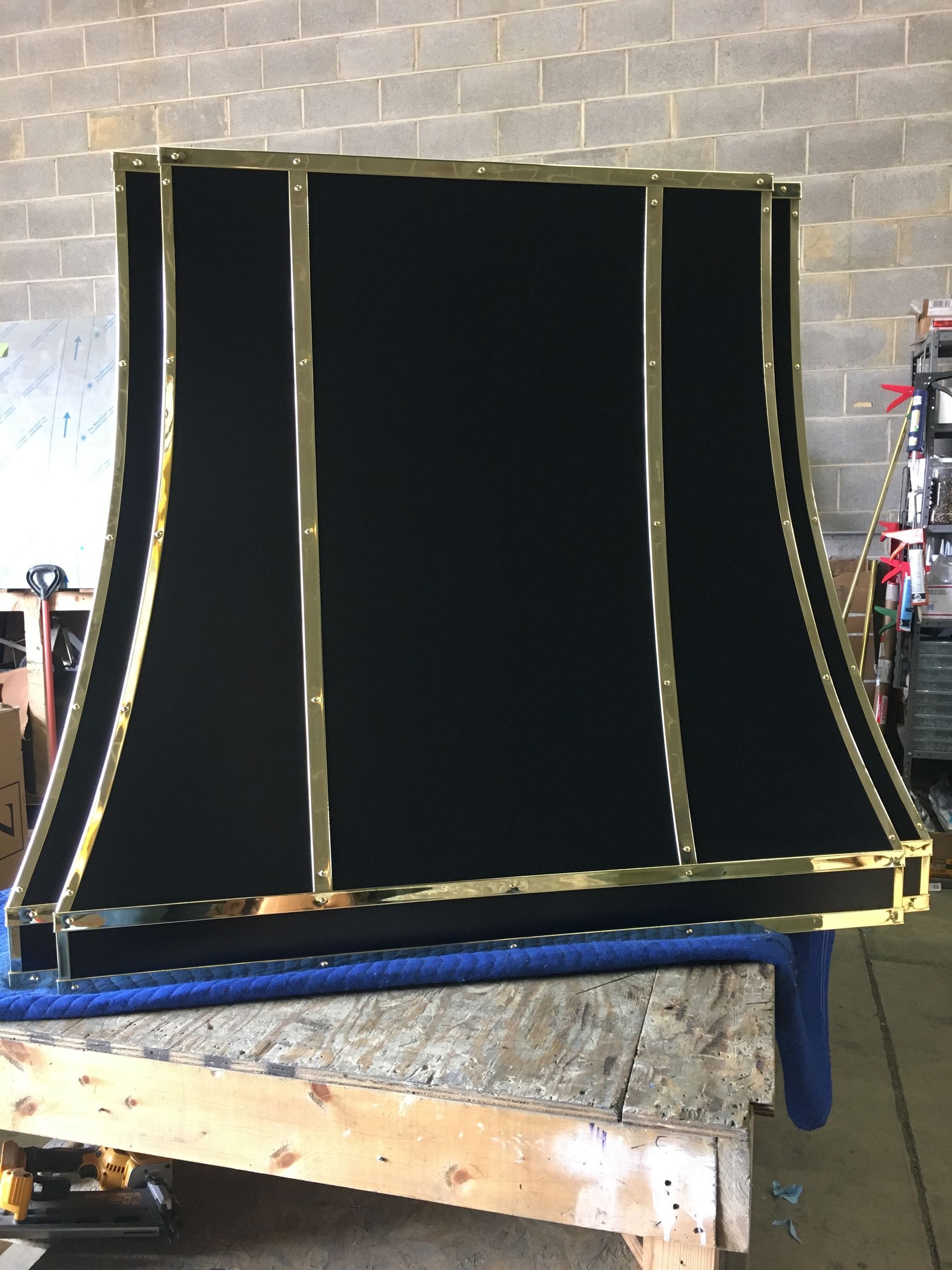 Black fabric panel framed in gold, standing on a blue table in a workshop.