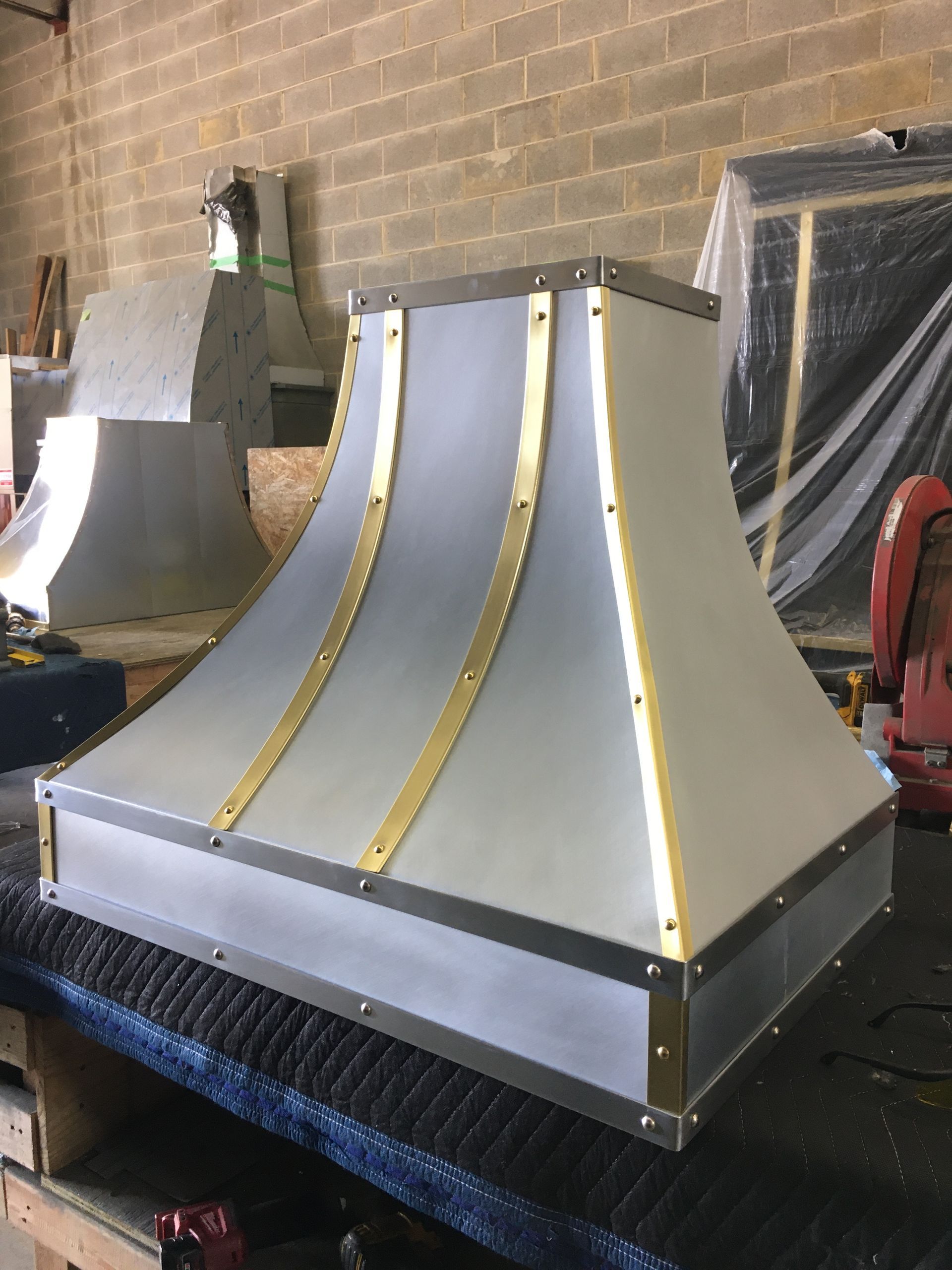 Silver metal duct or hood assembly with gold trim, sitting on a workbench in a workshop.