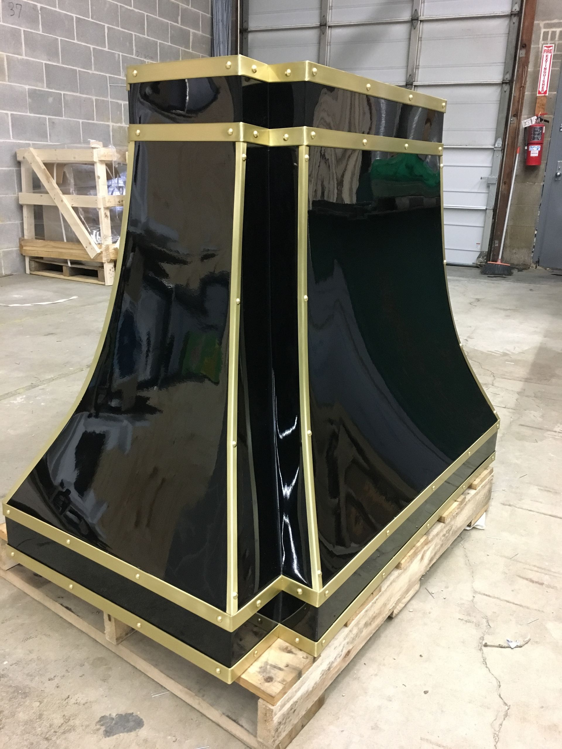 Glossy black industrial equipment housing with gold trim on a wooden pallet in a warehouse