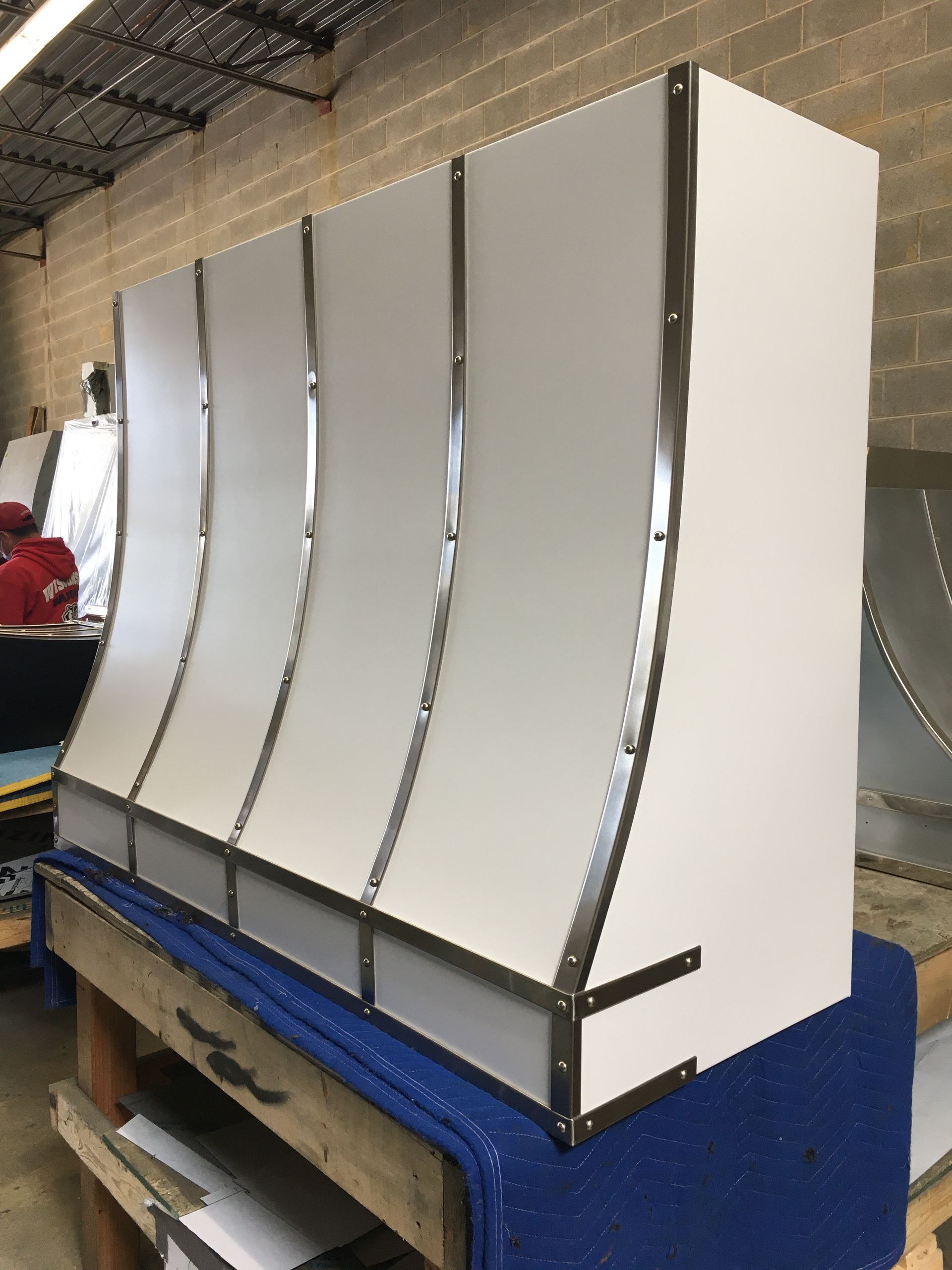Curved white metal panels mounted on a blue worktable in an industrial workshop