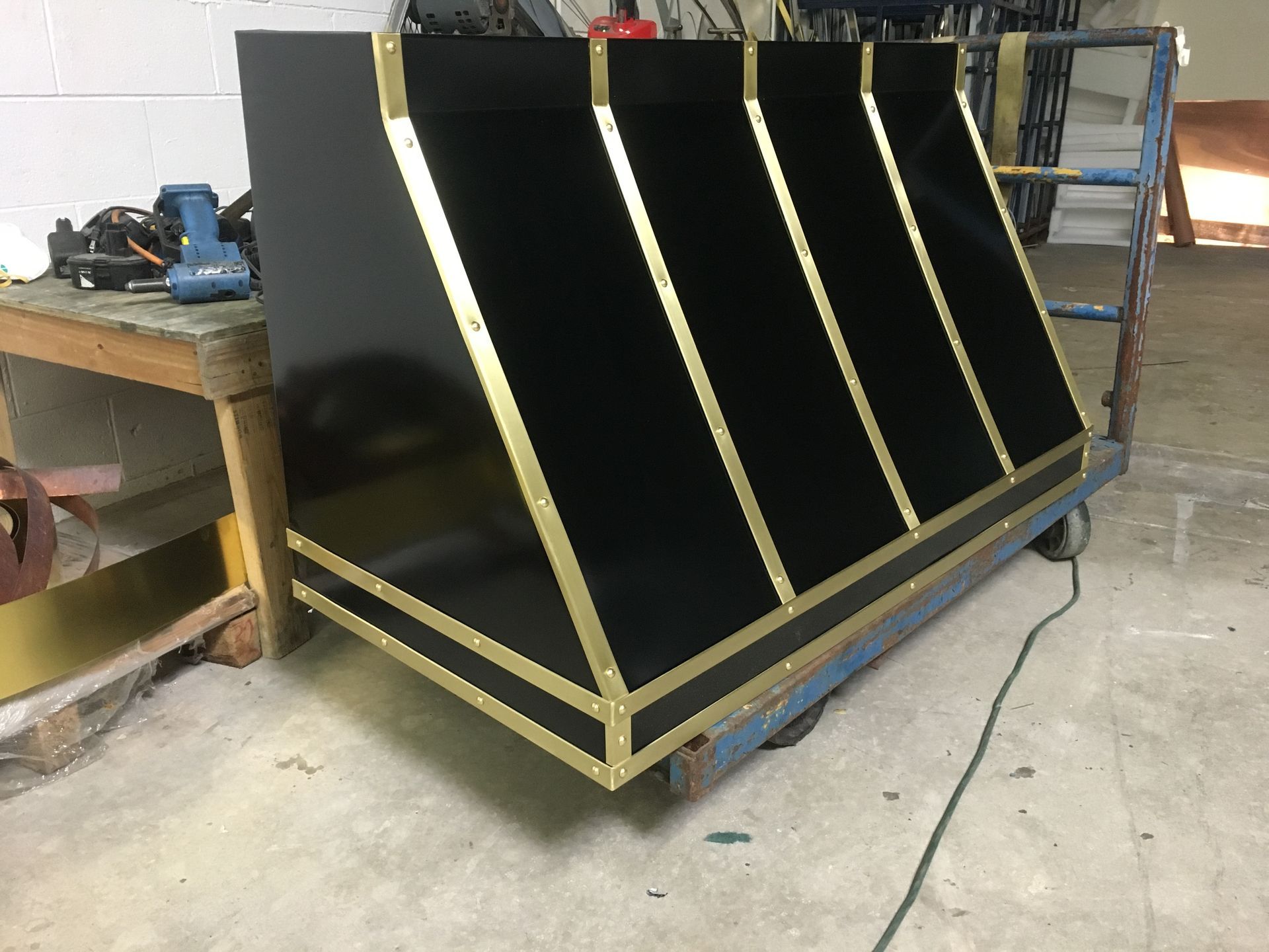 Black slanted metal panel with gold trim in a workshop, mounted on a blue cart.