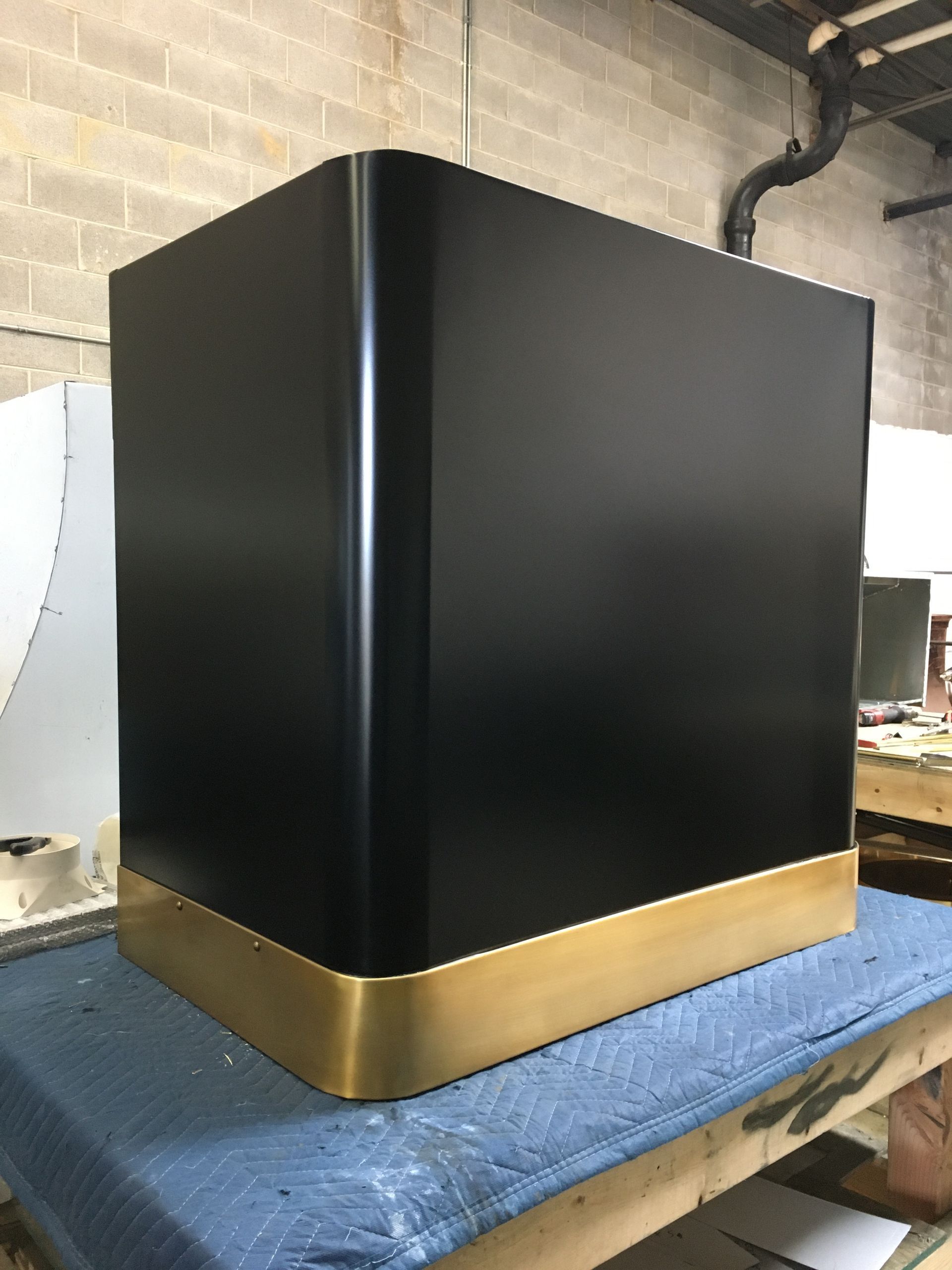 Black cabinet with gold base on a blue-covered table in a workshop.