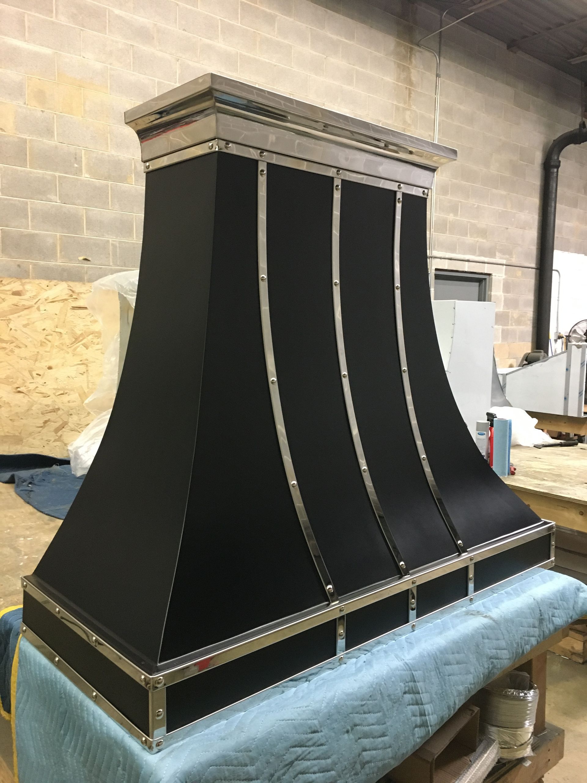 Black tapered metal hood on a blue padded workbench in an industrial workshop