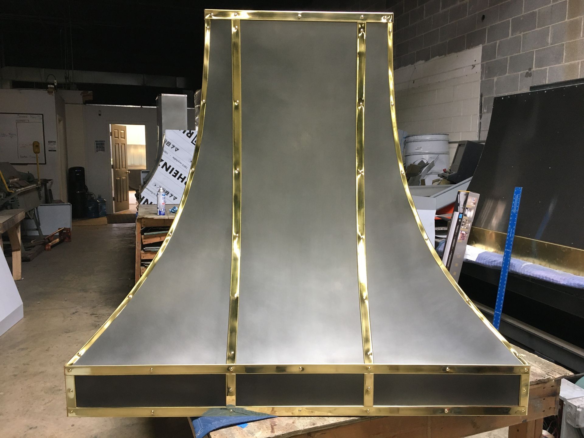 Gold-trimmed curved metal sculpture in a workshop with shelves and equipment in the background