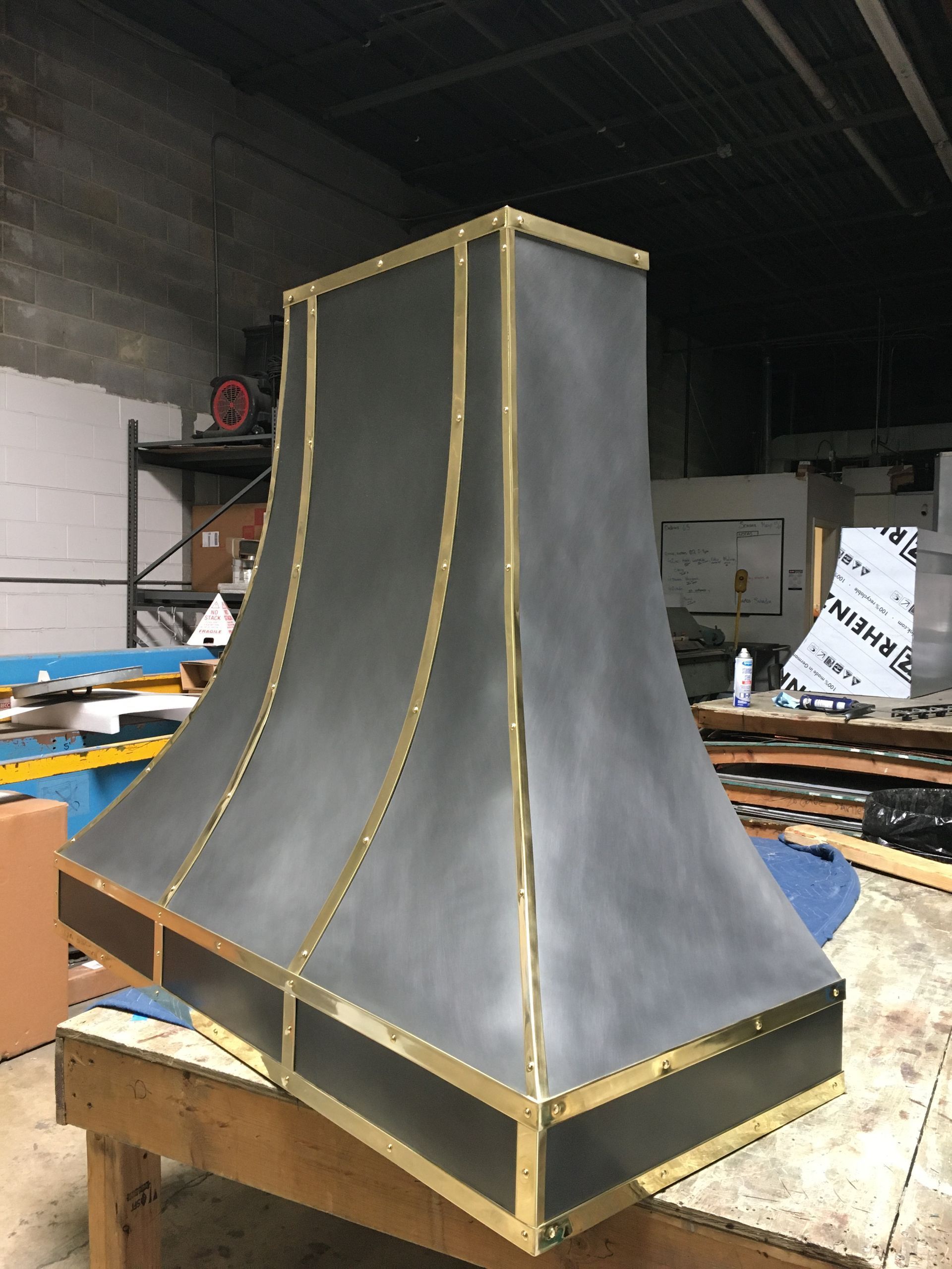 Large gray metal duct hood with gold trim on a workbench in a workshop