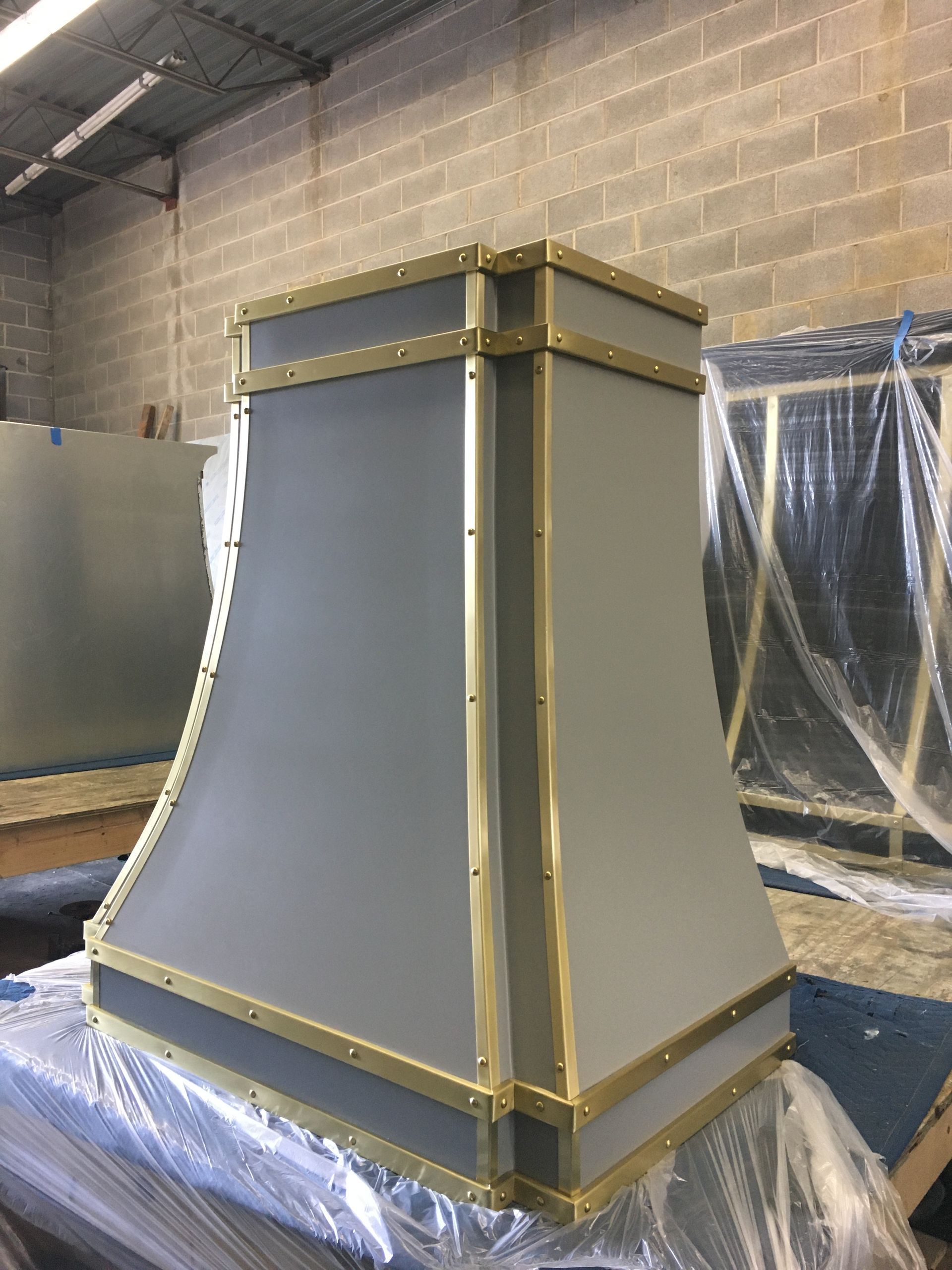 Gray decorative column in a workshop, with gold trim and protective wrap on the floor and wall.