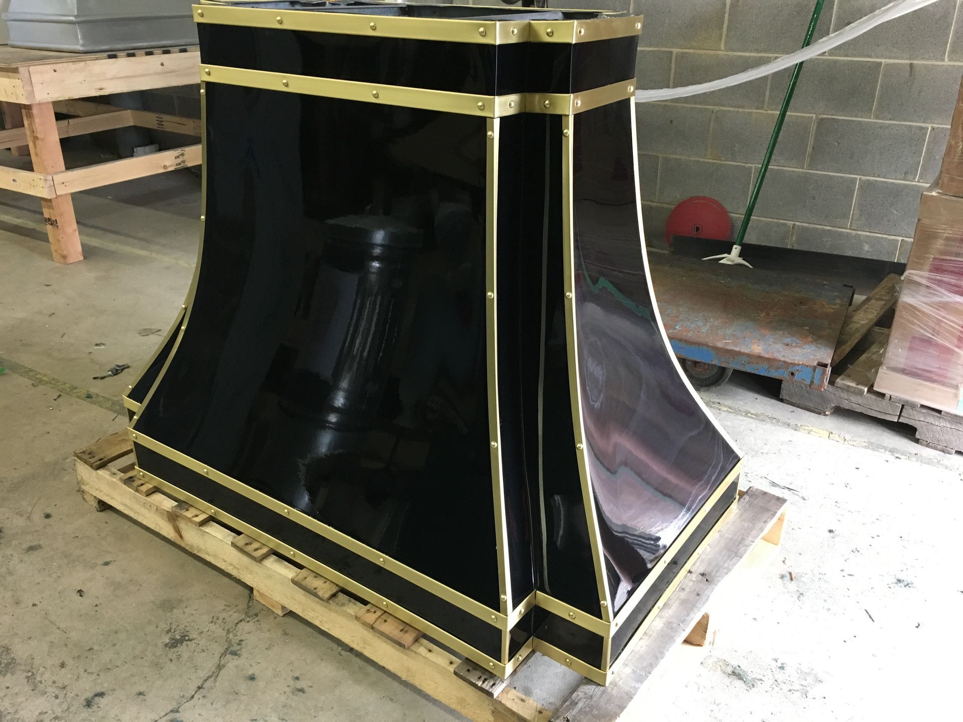 Black industrial machine housing with gold trim on a wooden pallet in a workshop, seen from the side