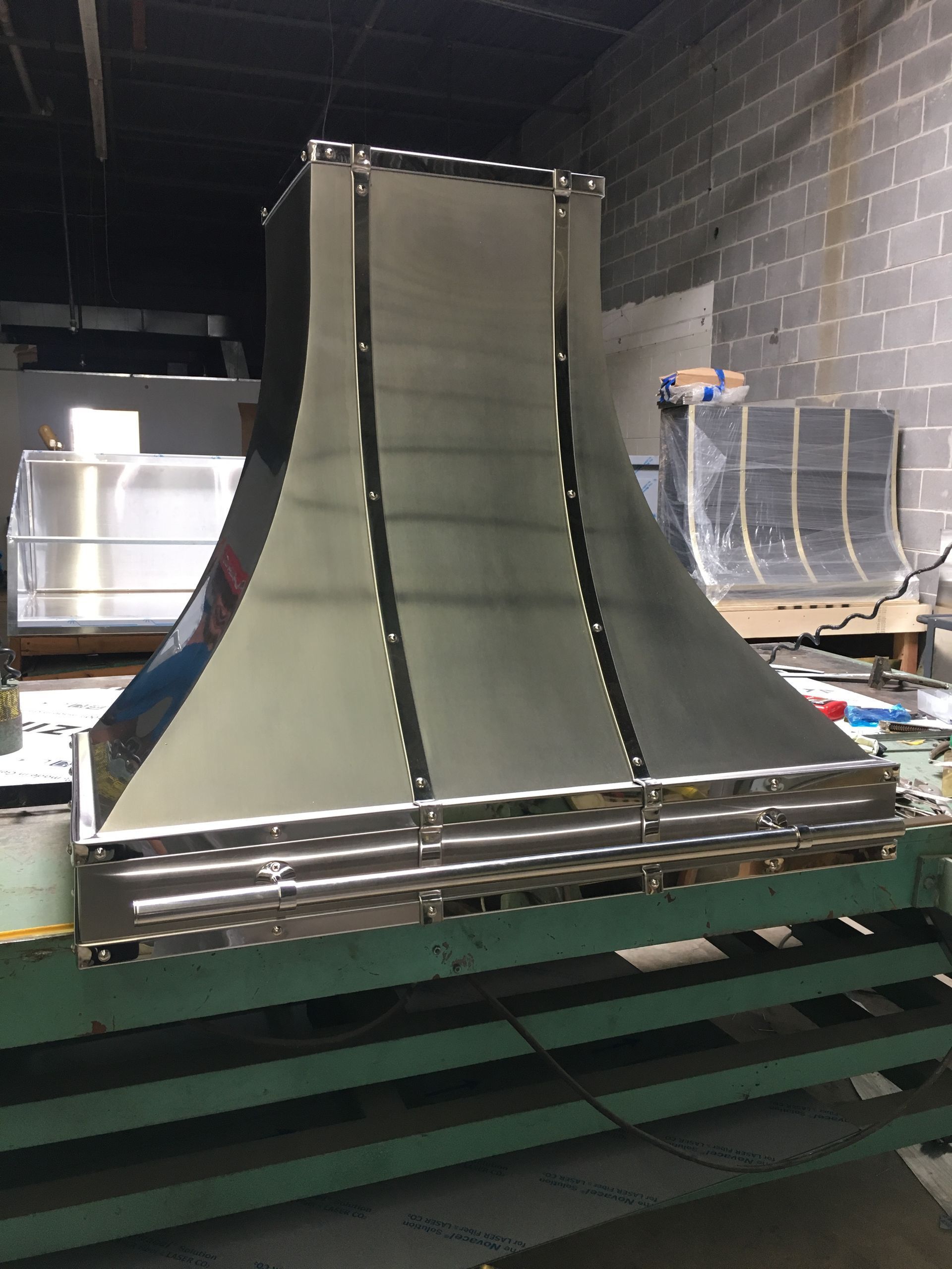Industrial metal ramp prototype in a workshop, with curved silver panels and black supports on a green platform.
