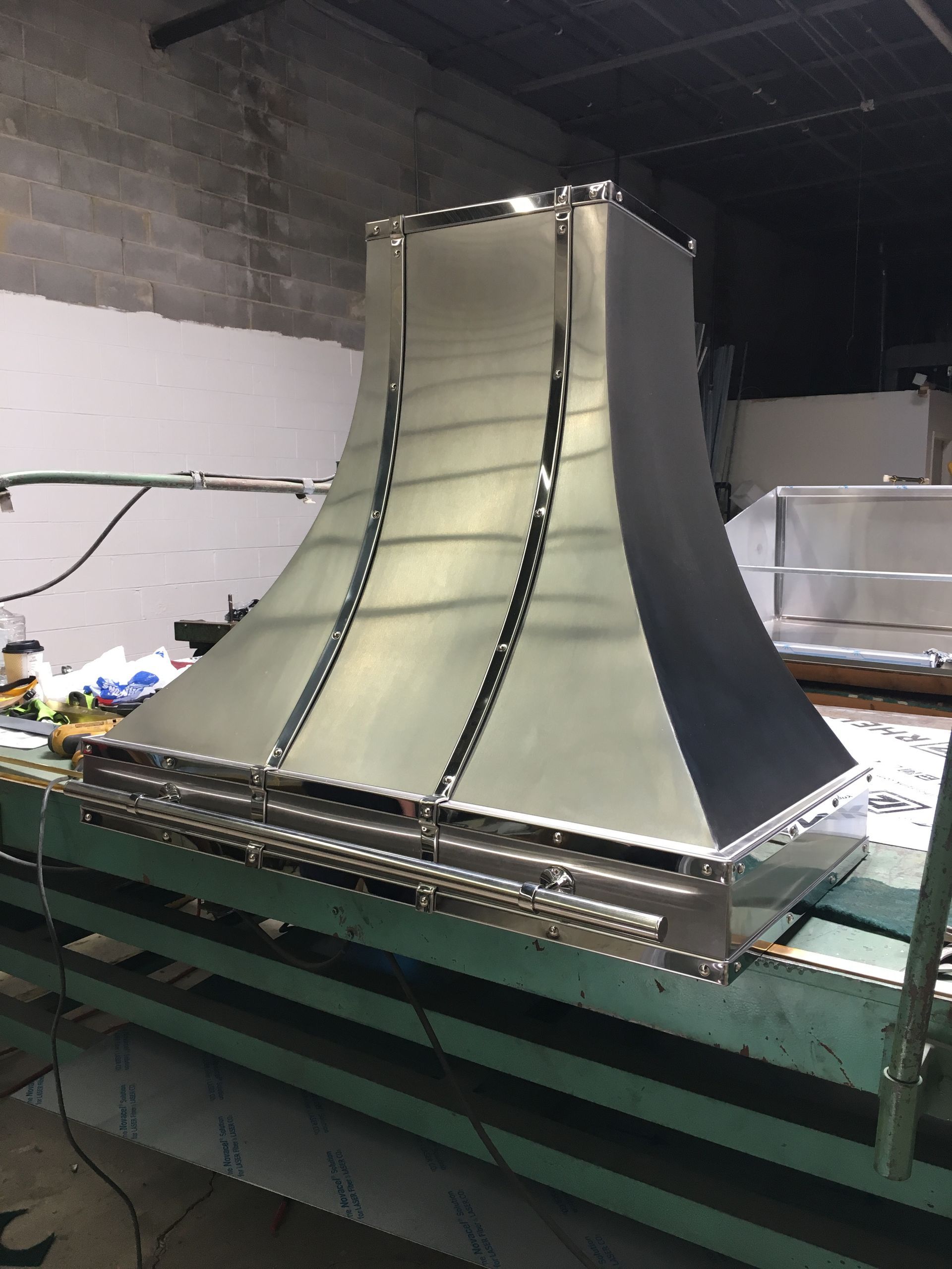 Metal duct or vent hood on a workbench in a workshop, with curved sides and reflective panels