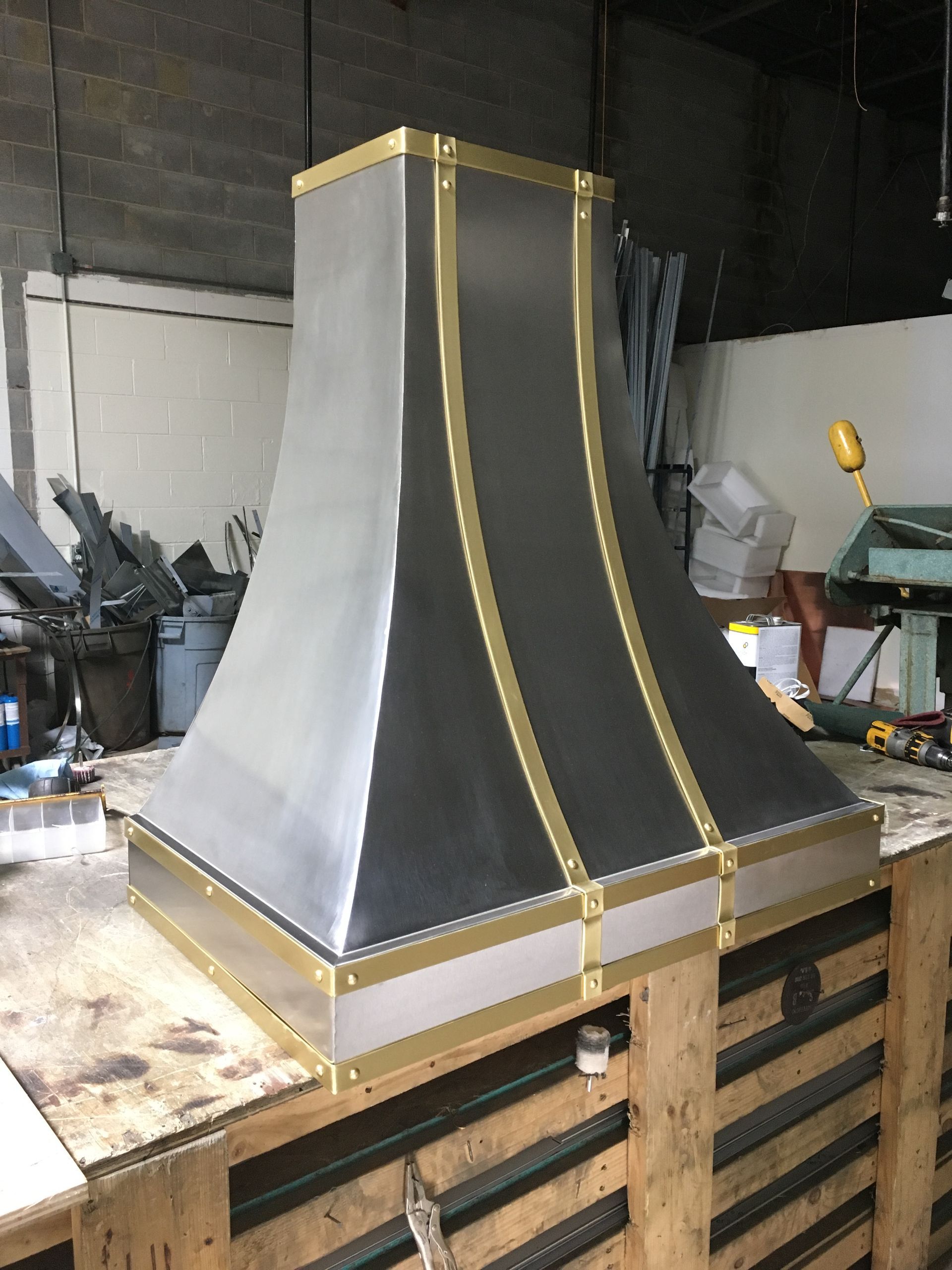 Large gray metal hood with gold trim on a wooden pallet in a workshop
