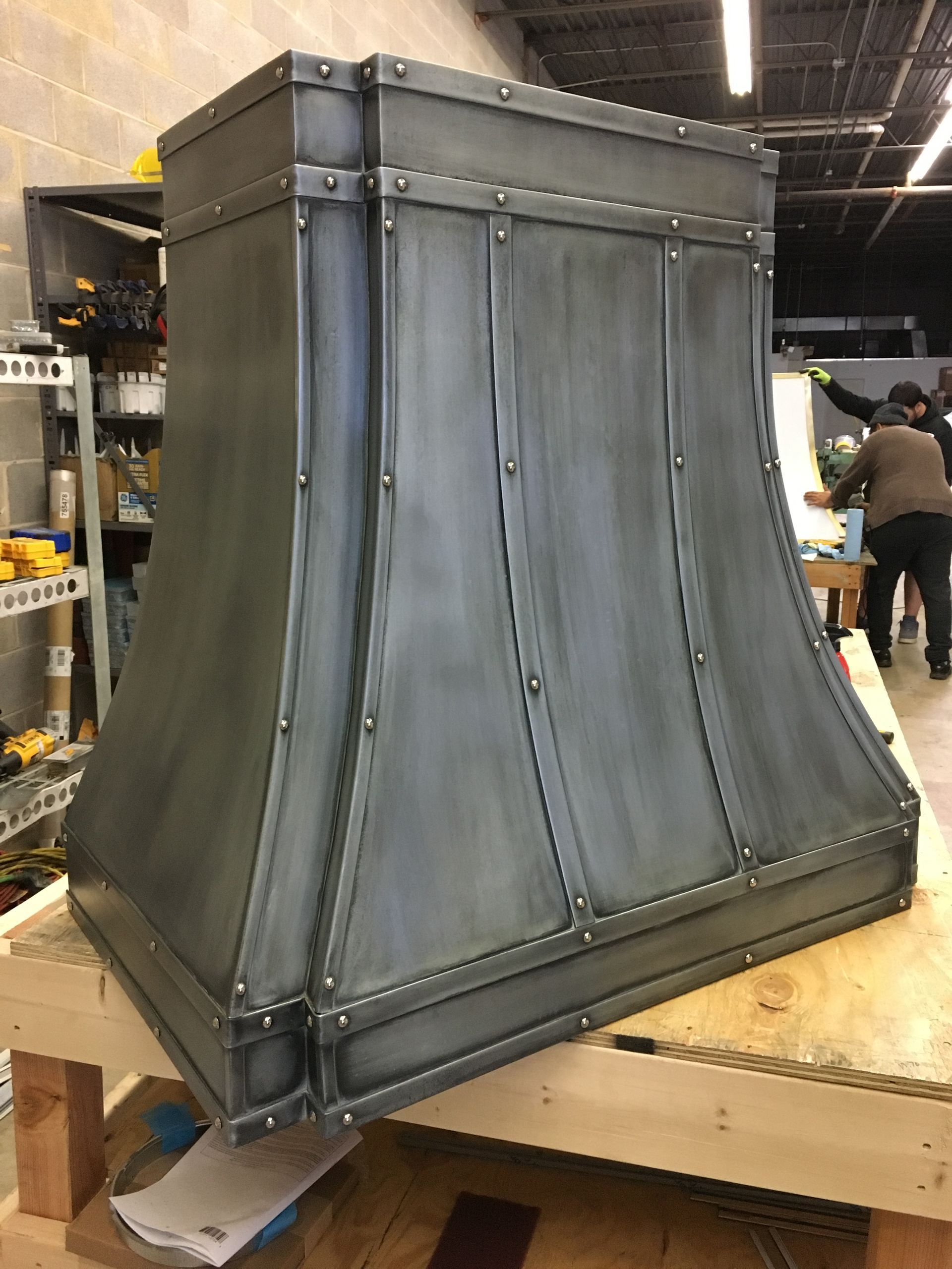 Gray metal vent hood on a workshop table, with curved sides and riveted seams.