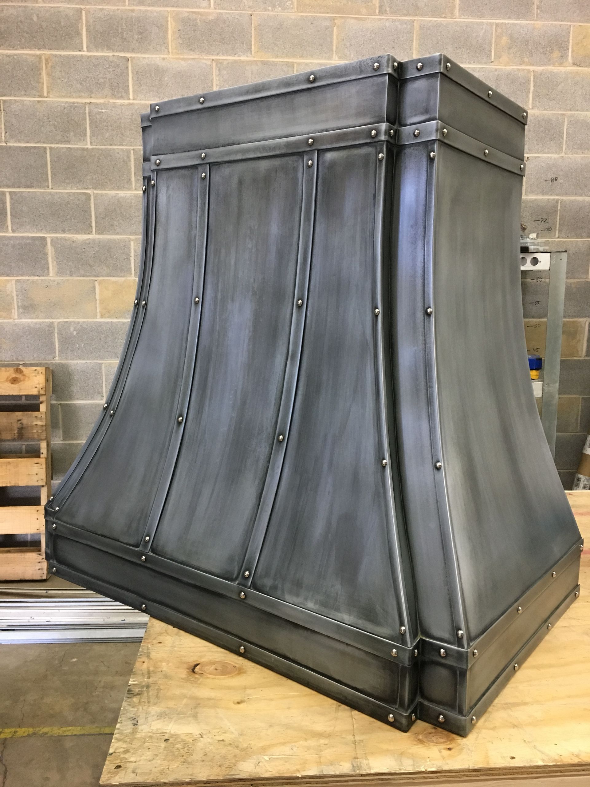 Large black metal duct or vent hood on a wooden pallet in an industrial workshop