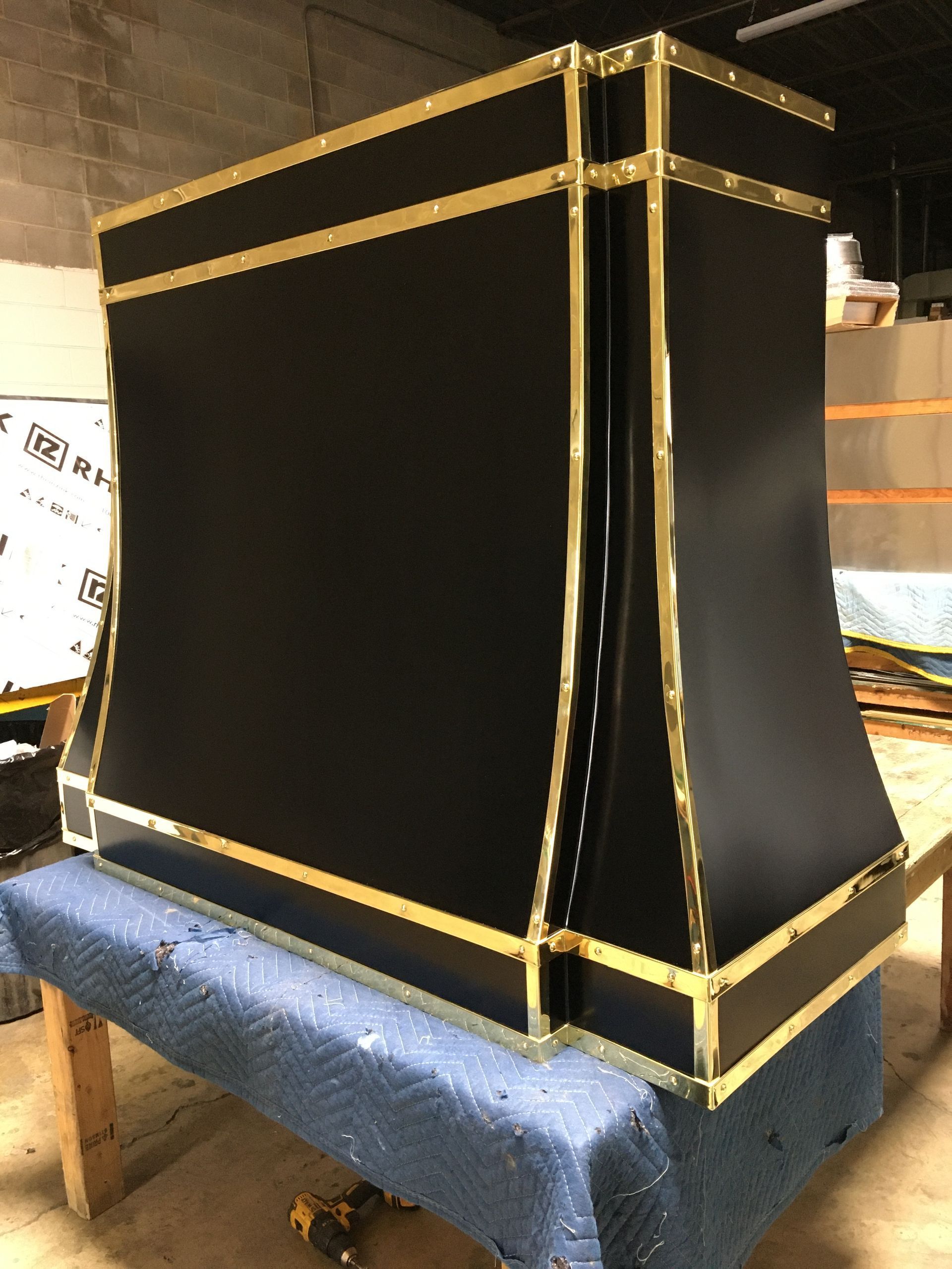 Black speaker cabinet with gold trim resting on a blue upholstered bench in a workshop