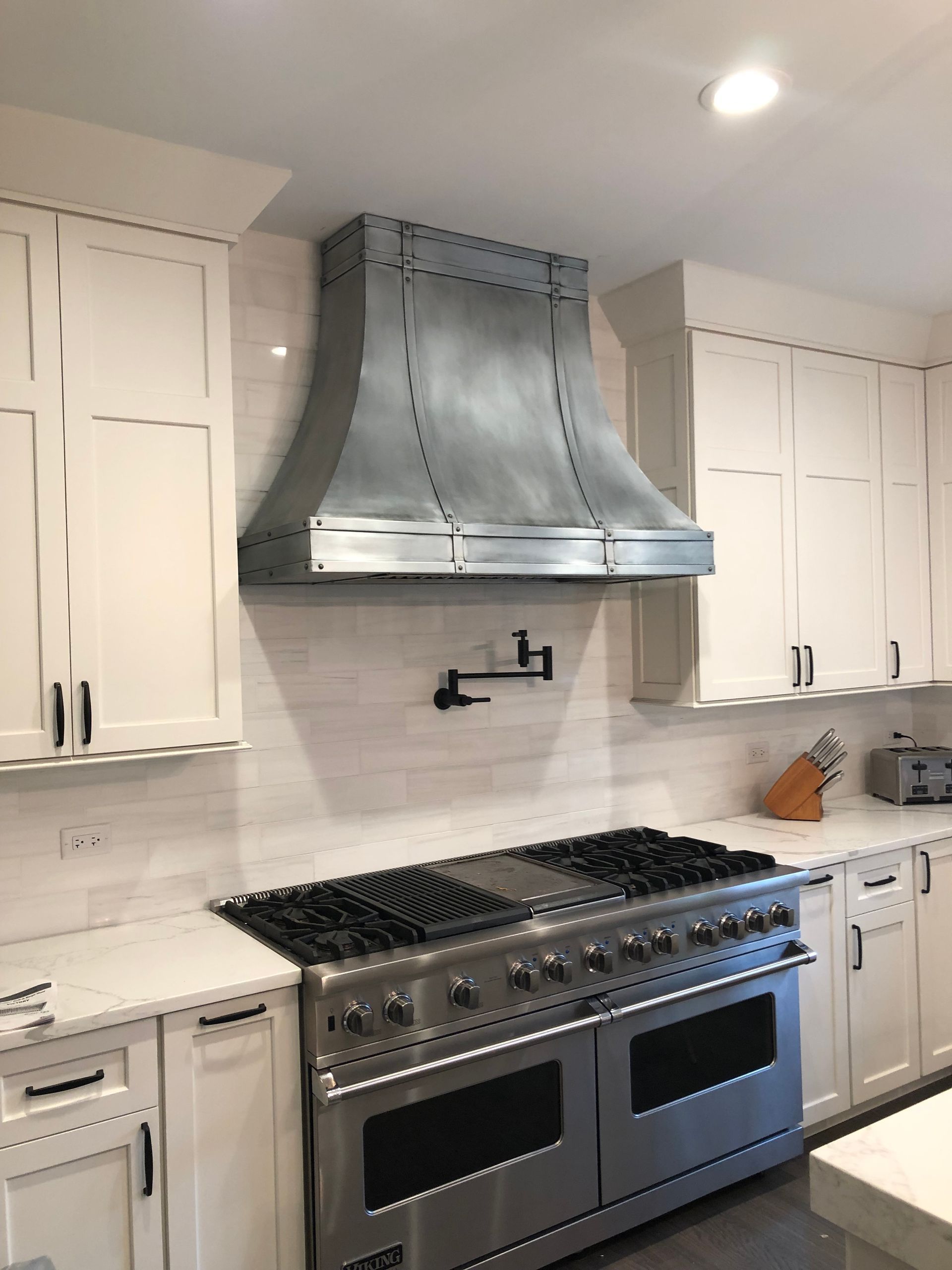 Modern white kitchen with stainless steel range, hood, and cabinets