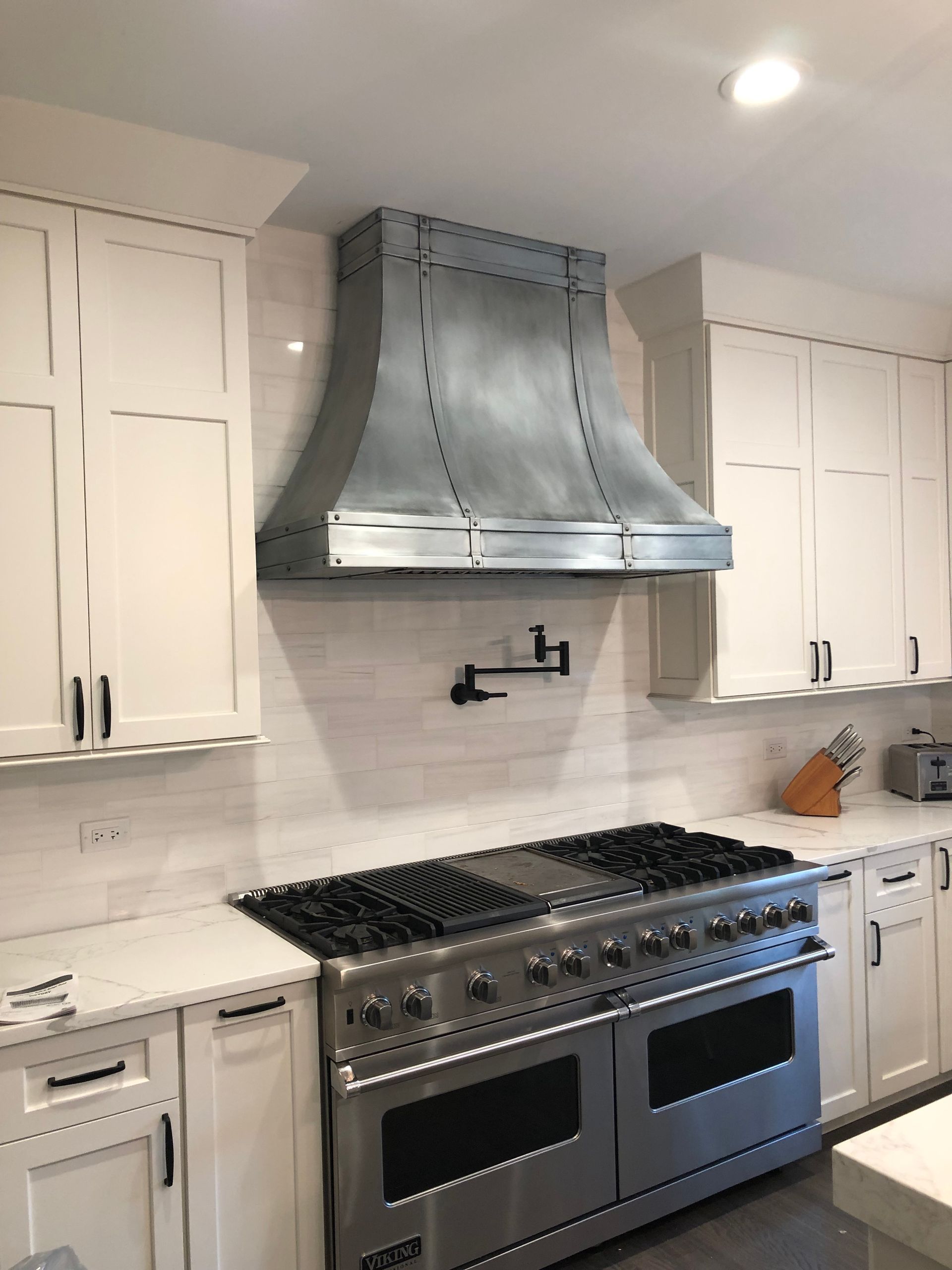 Modern white kitchen with stainless steel range and hood, white cabinets, and light countertops