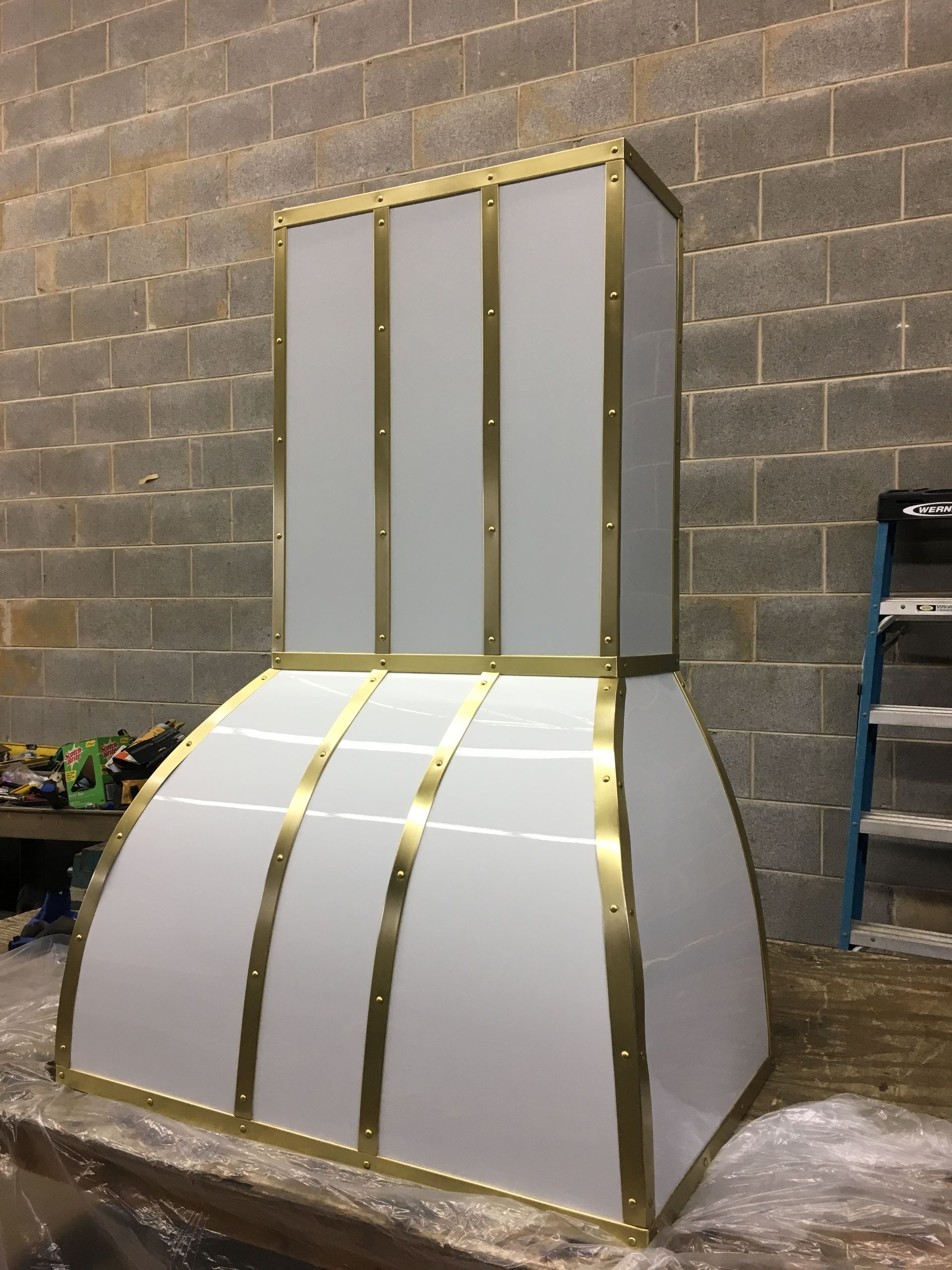 White and gold geometric sculptural installation against a cinderblock wall.