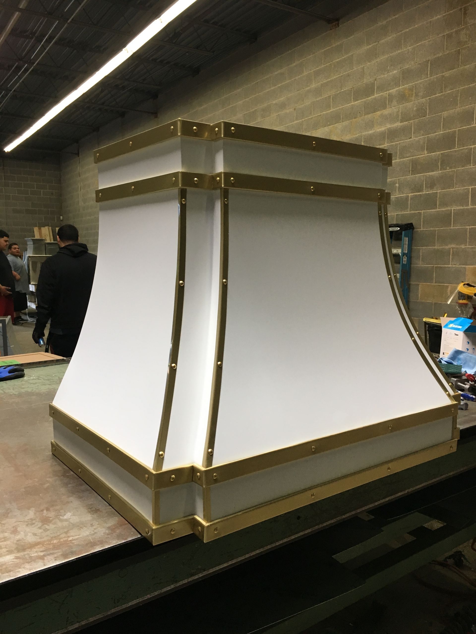 Large white hexagonal display booth with gold trim in a warehouse-like room