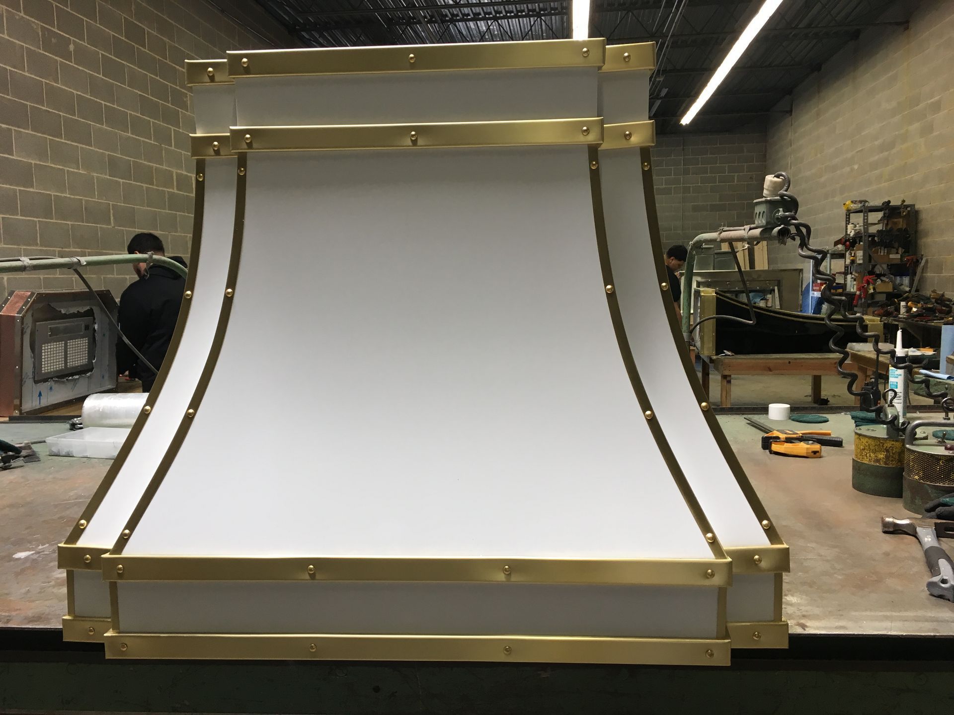 Large white curved panel with gold metal trim, standing in a workshop.