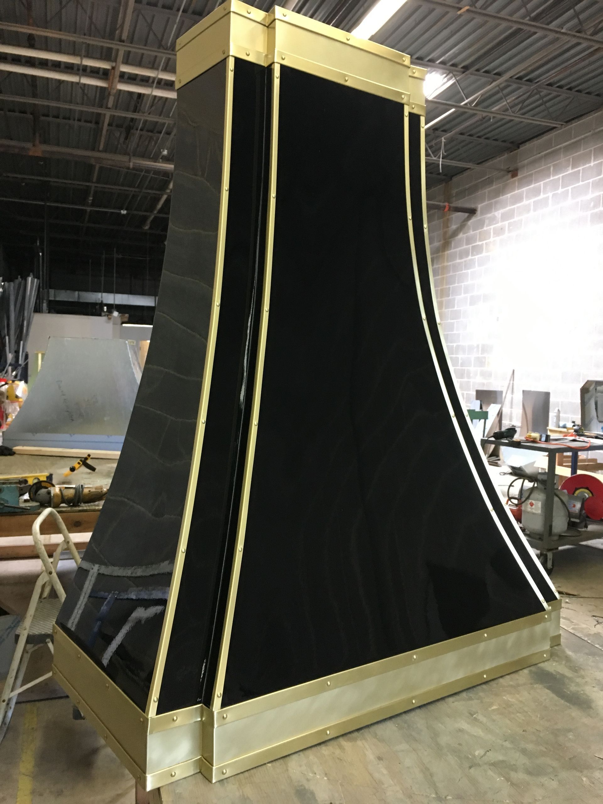 Large black tapered industrial structure with gold trim in a warehouse workshop.