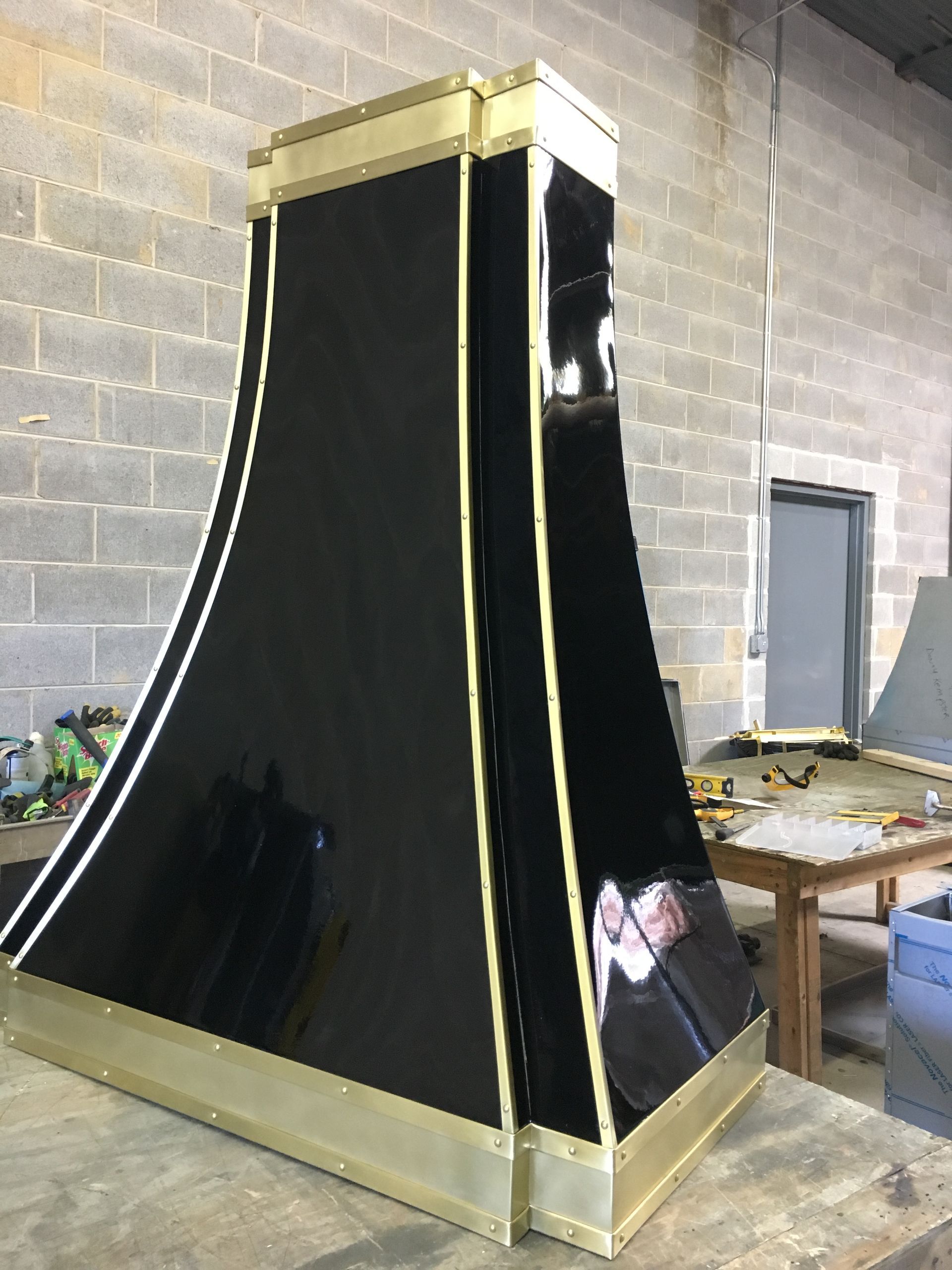 Black and gold coffin-shaped display or prop standing in a workshop against a brick wall