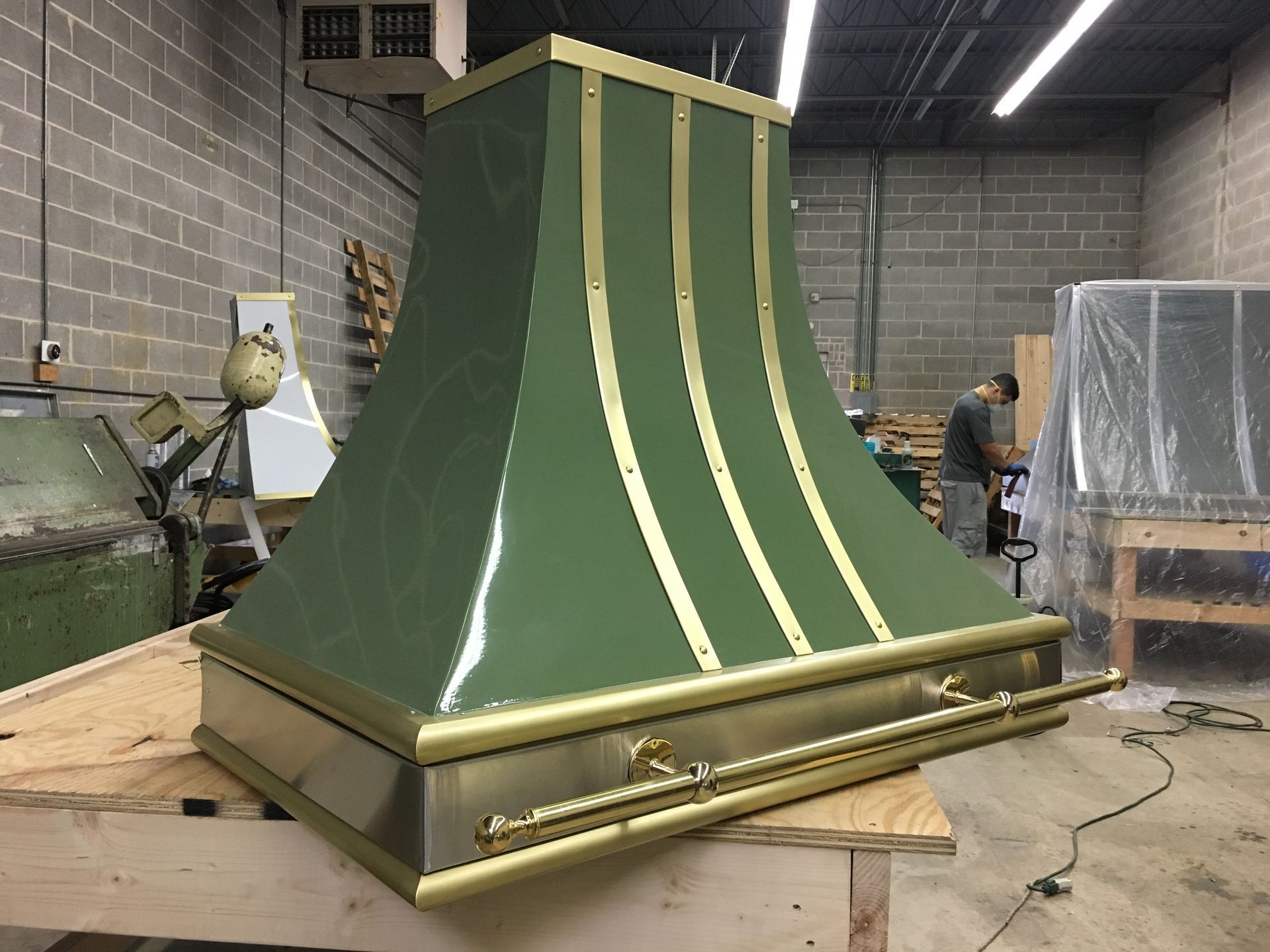 Green-and-gold decorative metal hood in a workshop, mounted on a wooden crate