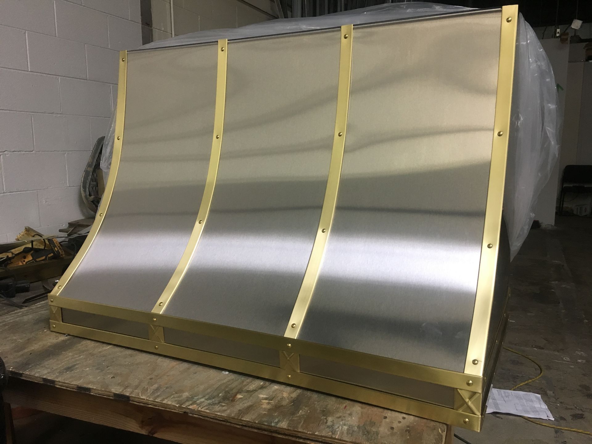 Large curved metal panel with yellow straps, leaning on a wooden pallet in a workshop.