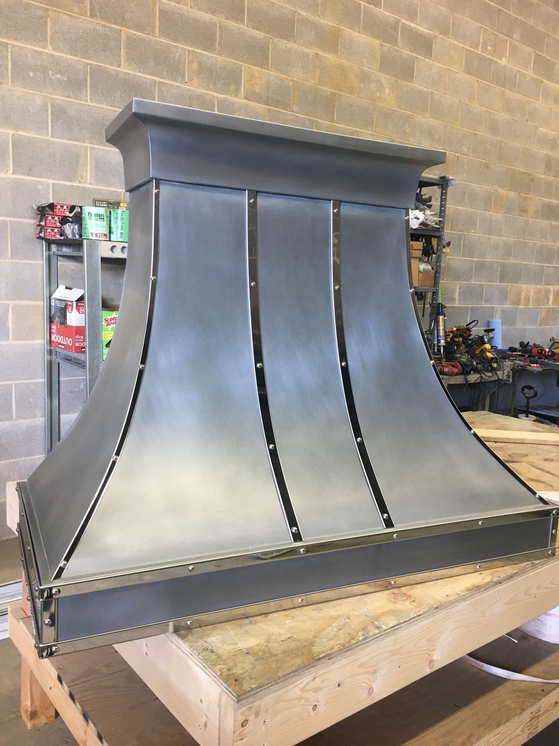 Large black metal chimney hood with riveted seams on a wooden pallet in a workshop.