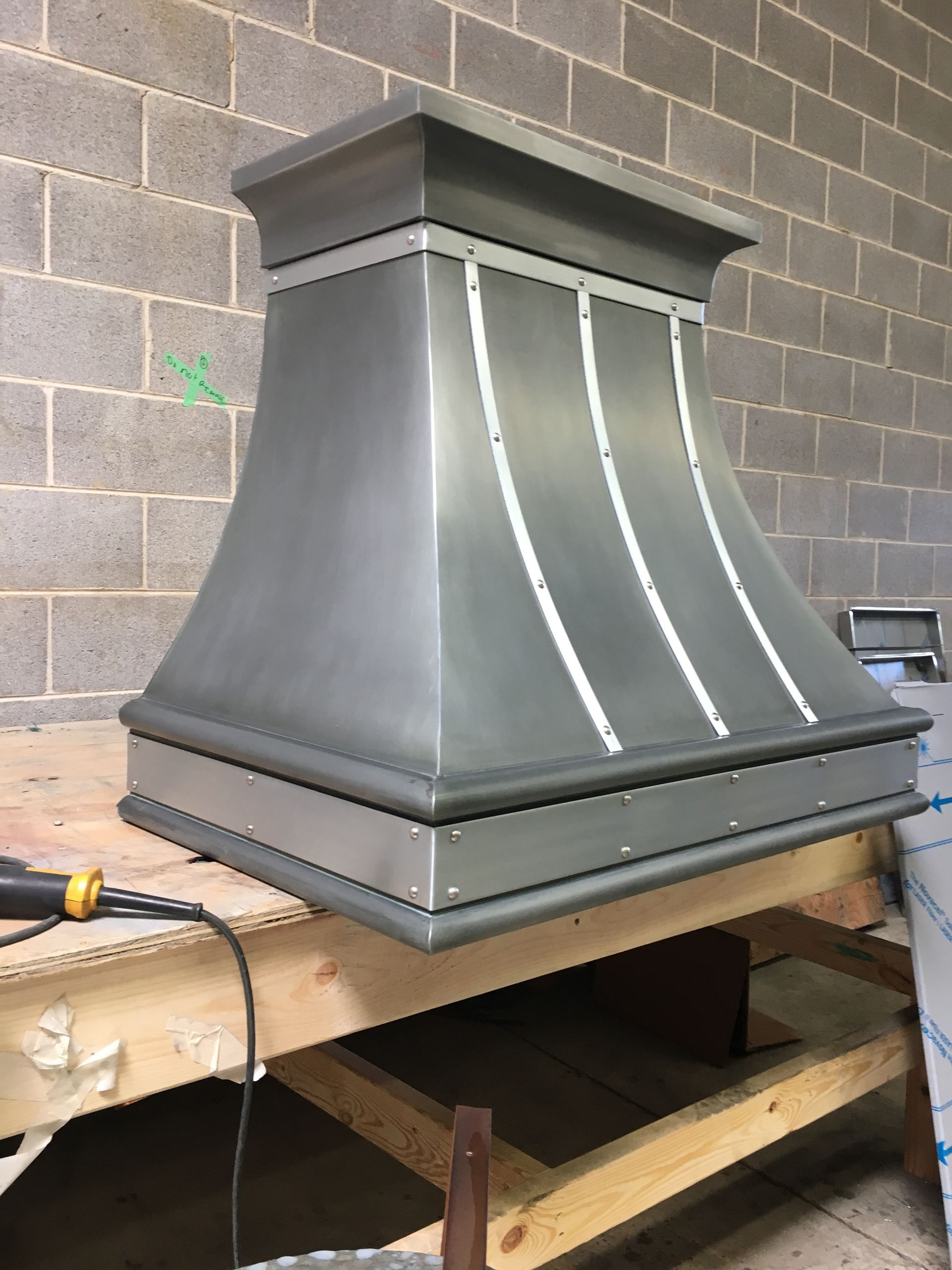 Metal chimney cap on a workbench against a cinder block wall