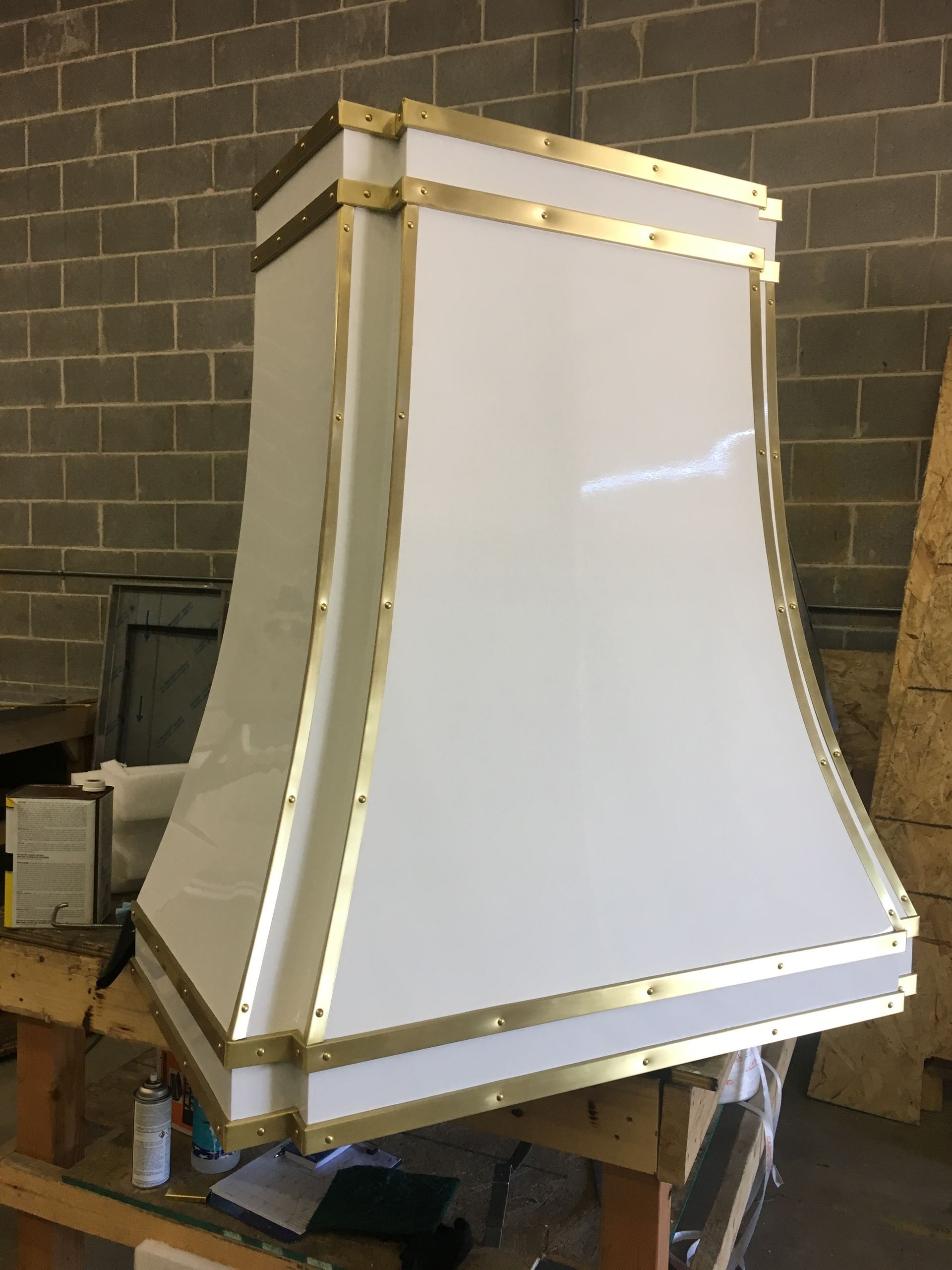 White curved display panel framed with gold trim in a workshop against a brick wall