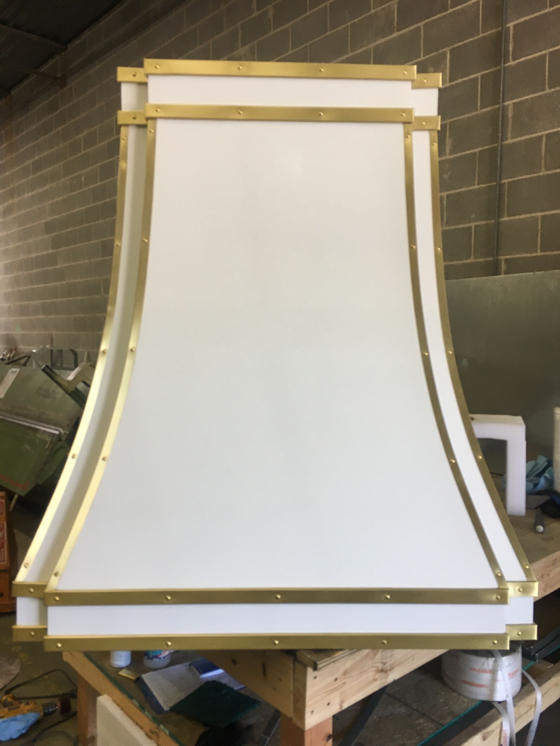 Large white curved panel with gold trim mounted on a workbench in a workshop