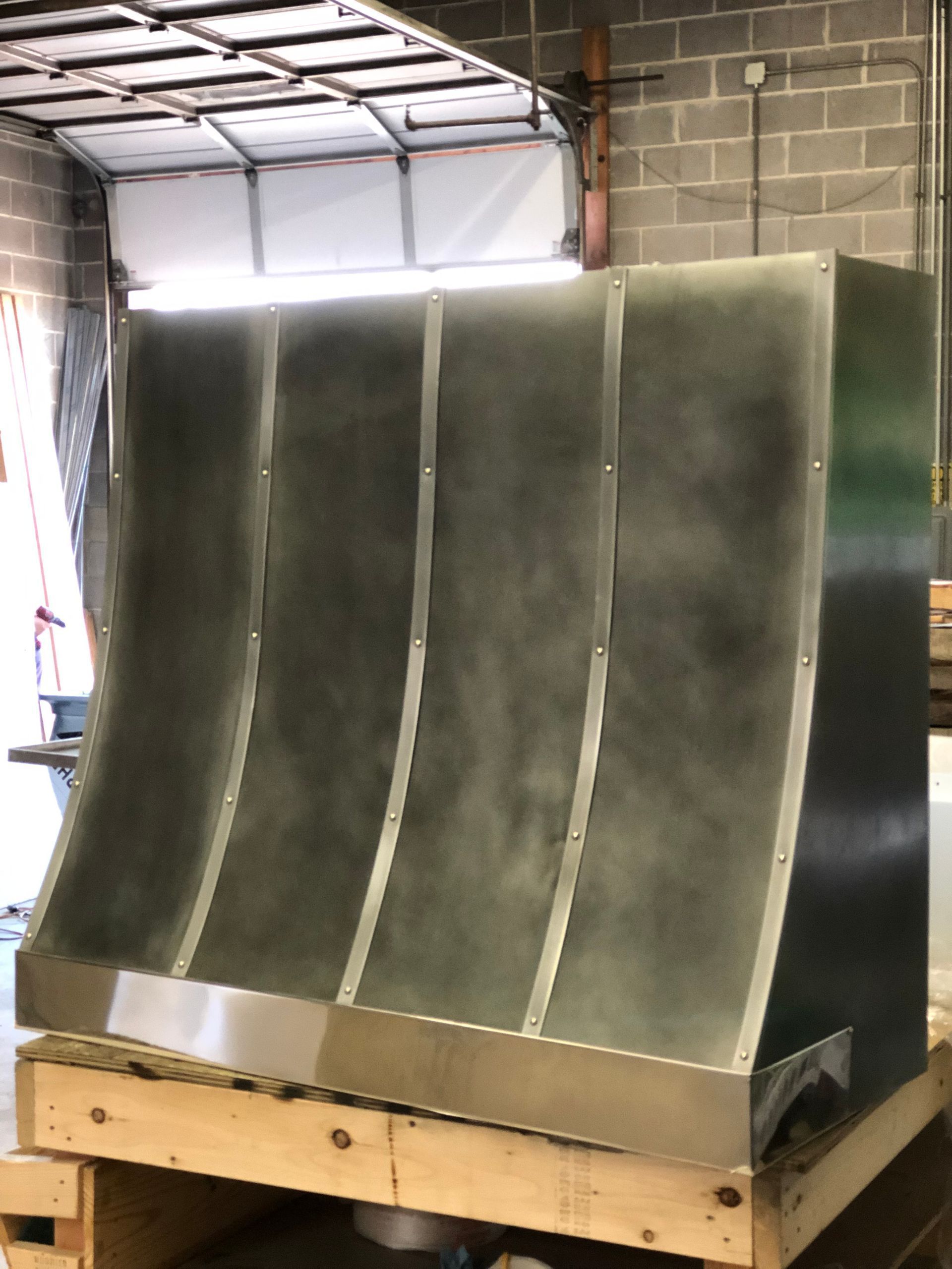 Large curved metal duct or hood on a wooden pallet inside a workshop/warehouse.