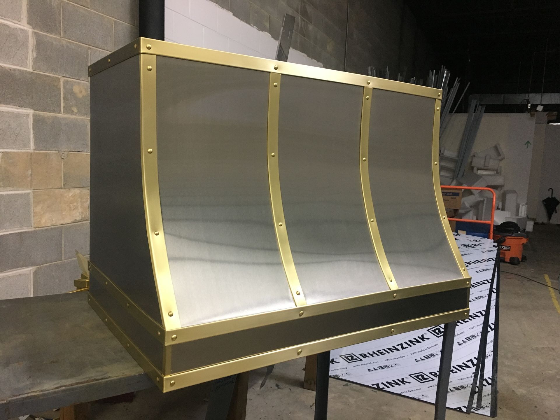 Gold-framed metallic display case with a curved silver front in a workshop setting