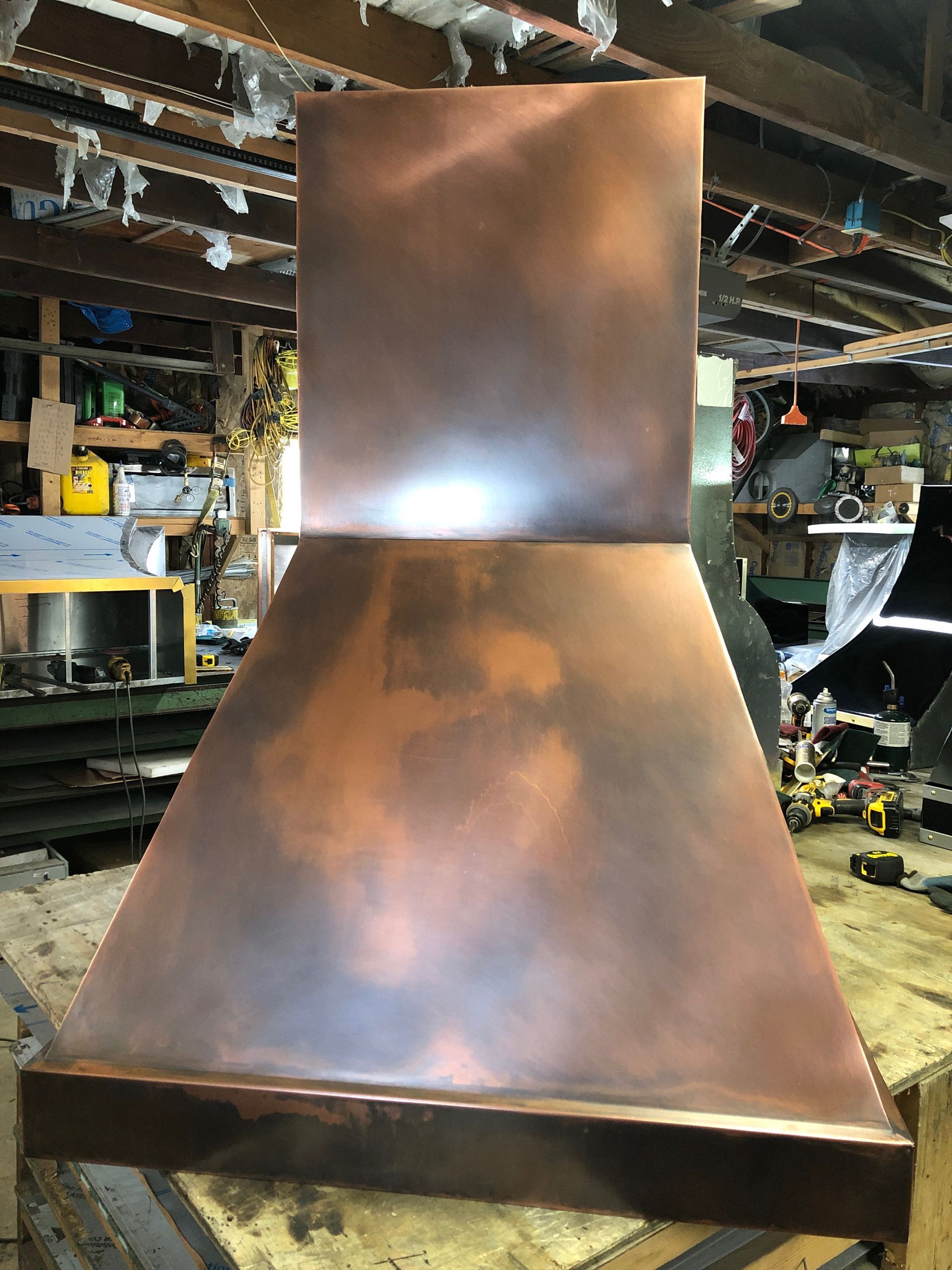Copper range hood with a square chimney in a workshop setting