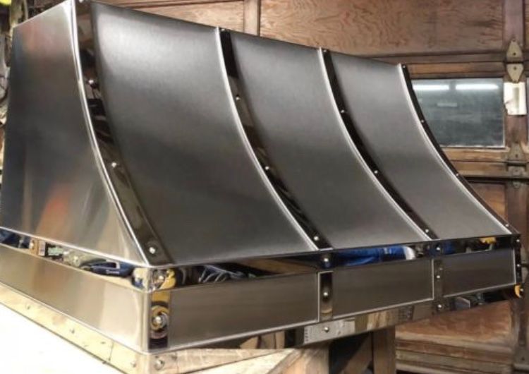 Shiny curved metal ventilation hood with four panels in an industrial workshop