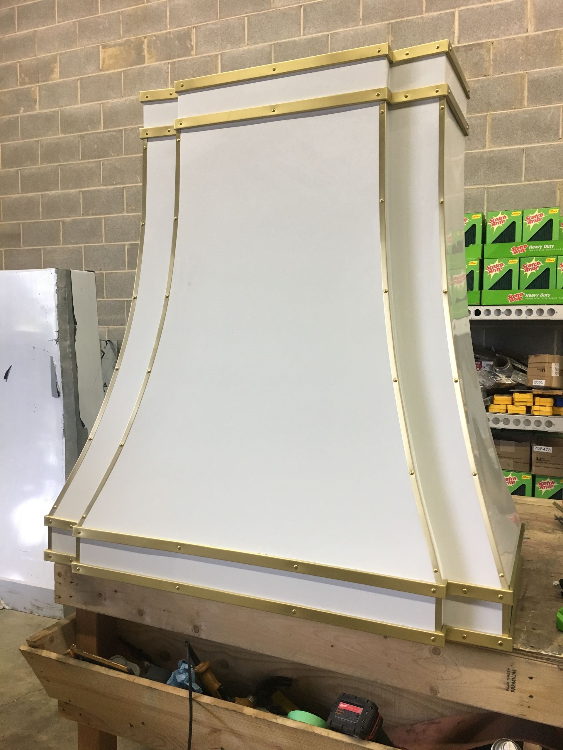 Large white decorative mantel or hood with gold trim in a workshop against a cinderblock wall