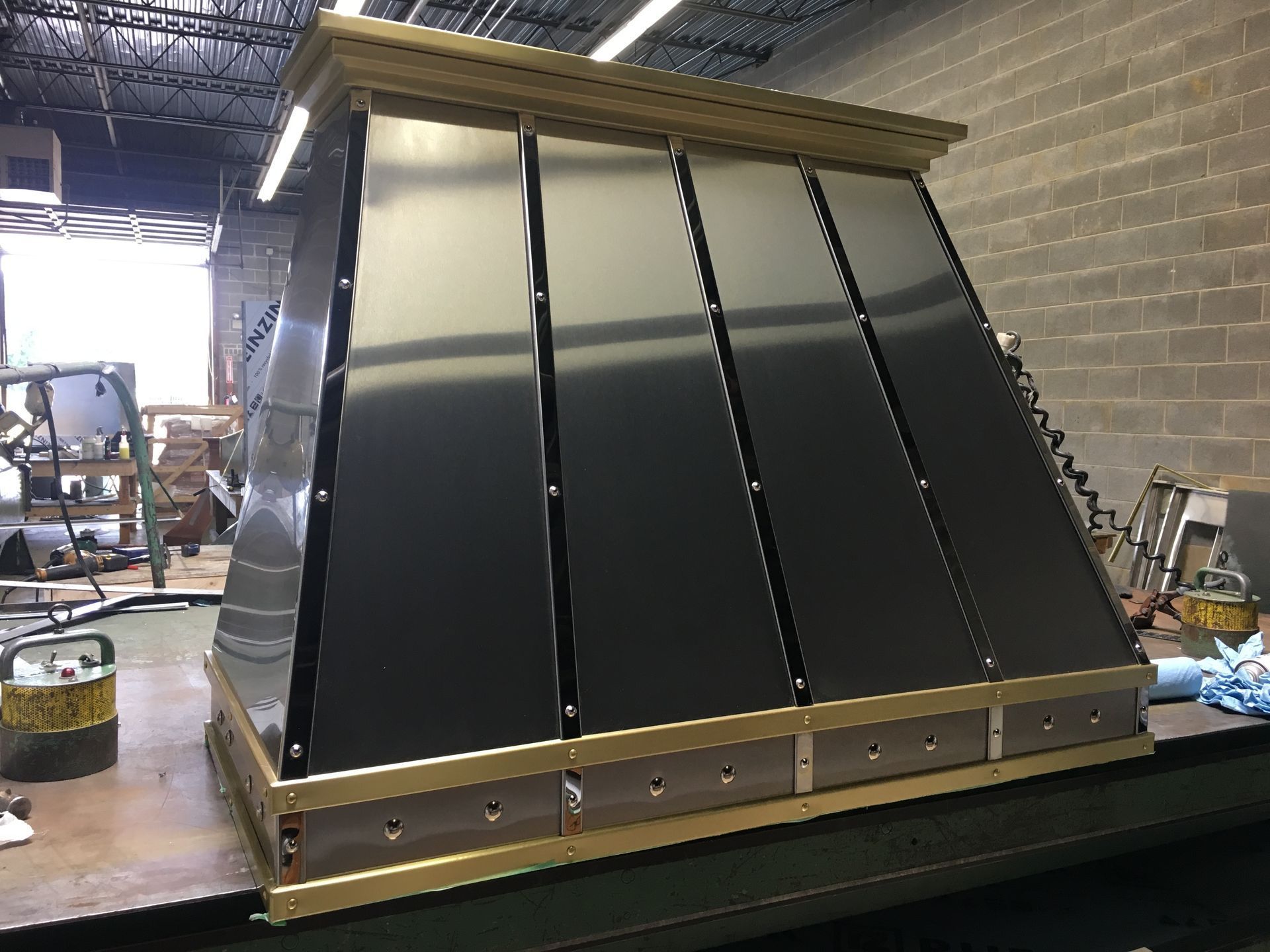 Large black metal panel assembly with wooden frame in a workshop, leaning against a wall.